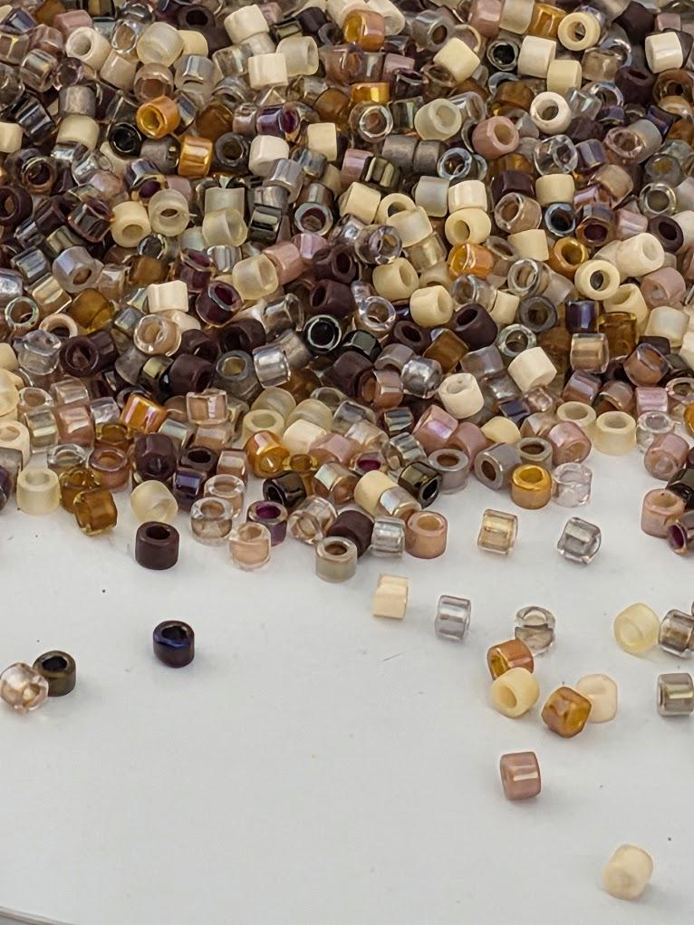 A large pile of multicolored beads, including various shades of brown, beige, and other colors, scattered across a white surface.