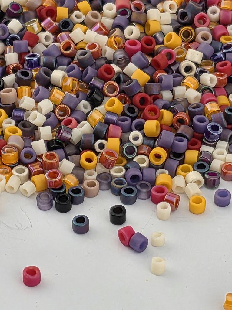 A colorful pile of multicolored beads, including red, yellow, purple, and white, scattered on a dark surface.