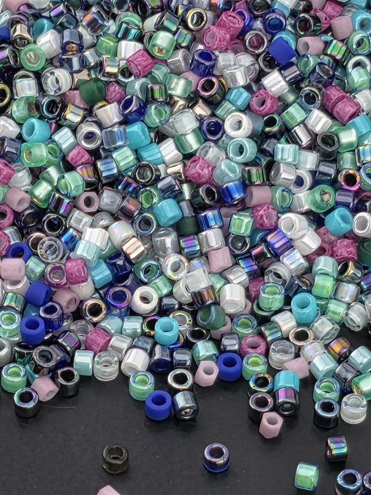 A colorful pile of multicolored beads, including various shades of blue, green, purple, and pink, scattered on a dark surface.