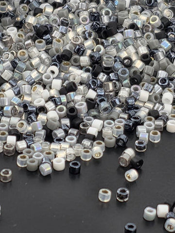a large pile of various colored beads, including black, white, and silver, scattered on a dark surface.