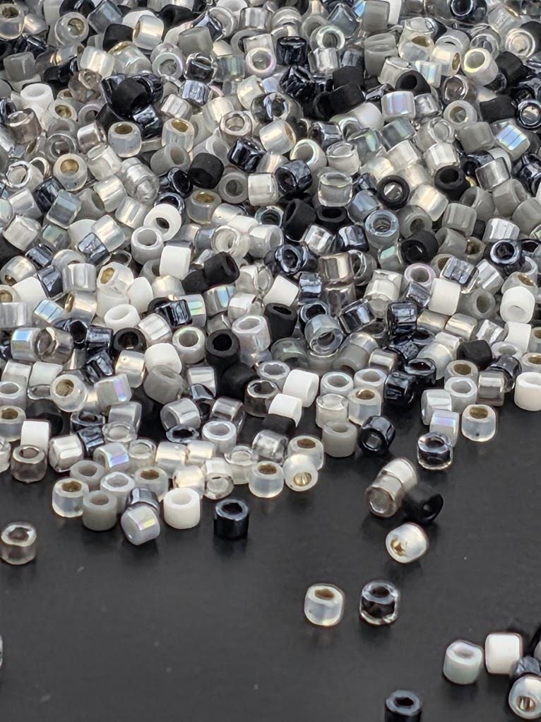 a large pile of various colored beads, including black, white, and silver, scattered on a dark surface.
