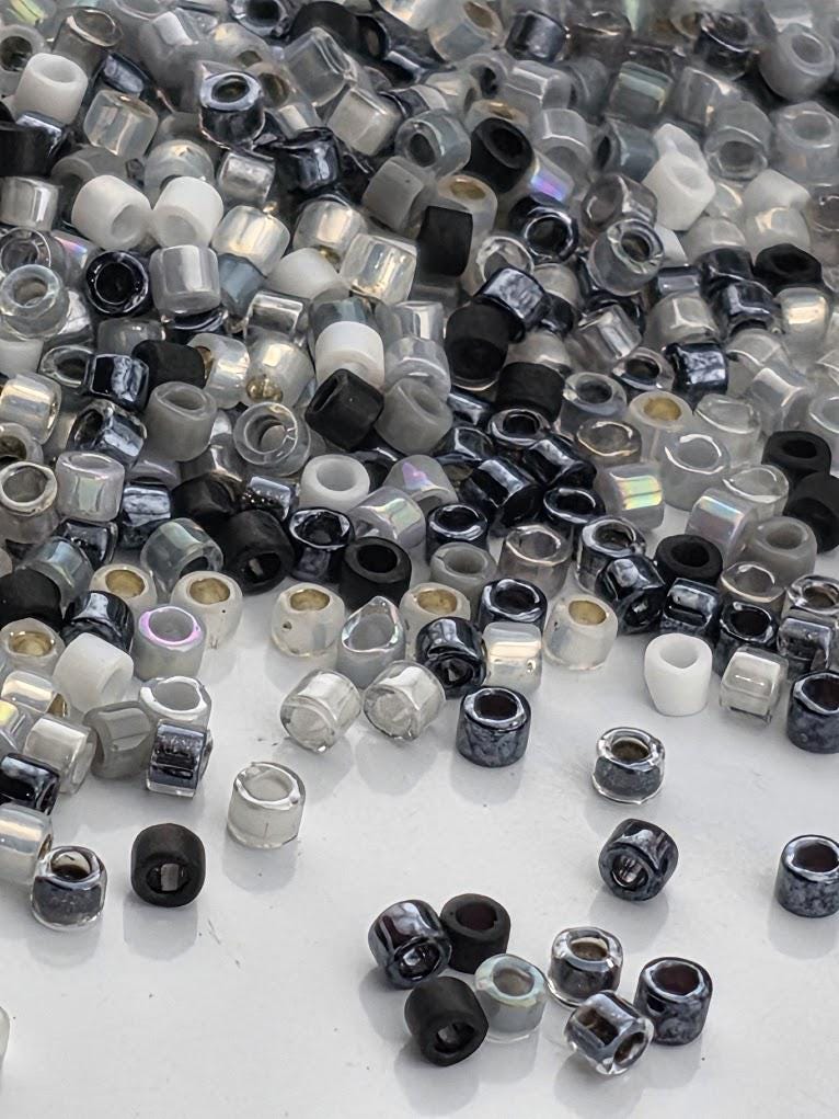 a large pile of various colored beads, including black, silver, and white beads, scattered on a white surface.