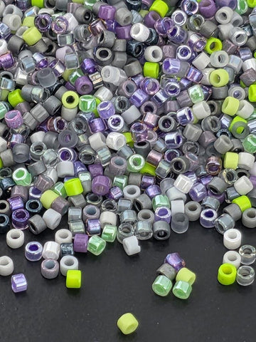 The image is a close-up of a pile of multicolored beads, including various shades of purple, green, and gray, scattered on a dark surface.