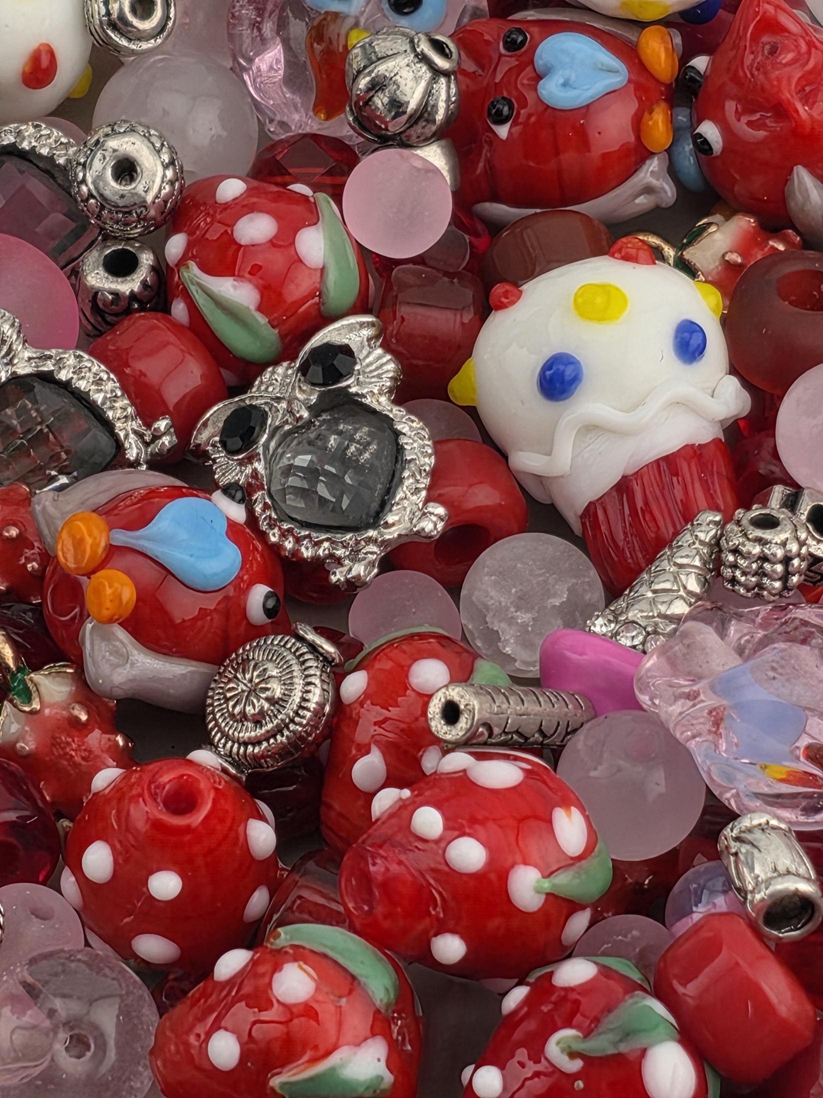 The image is a close-up of a collection of colorful beads, charms, and other small objects, including a white and yellow object resembling a clown, red and white polka dot objects, and various other shapes and designs.