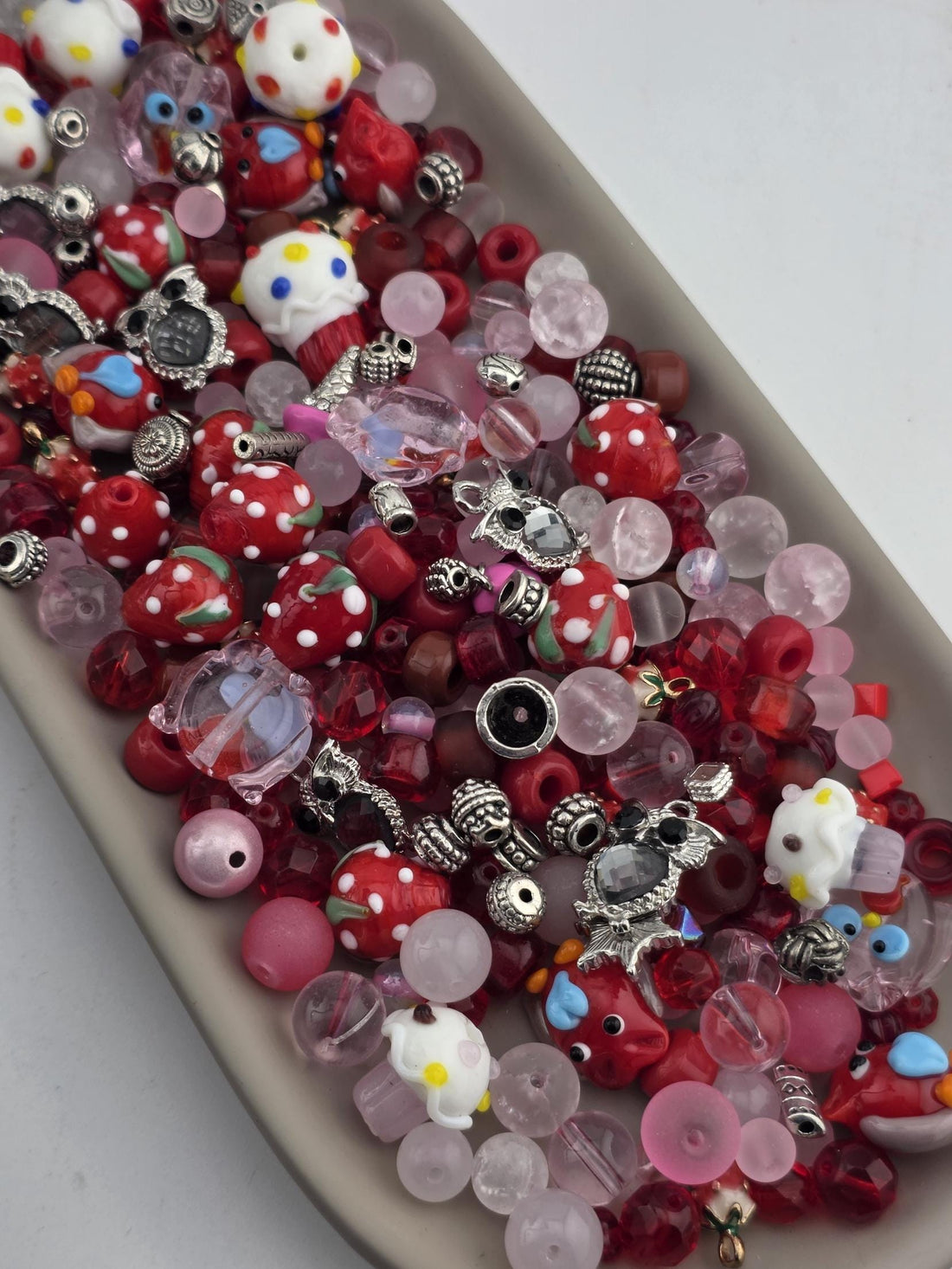 The image is a close-up of a collection of colorful beads, charms, and other small objects, including a white and yellow object resembling a clown, red and white polka dot objects, and various other shapes and designs.