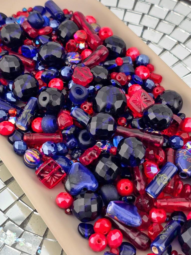 The image is a close-up of various colorful beads, including red, blue, and multicolored beads, scattered together.