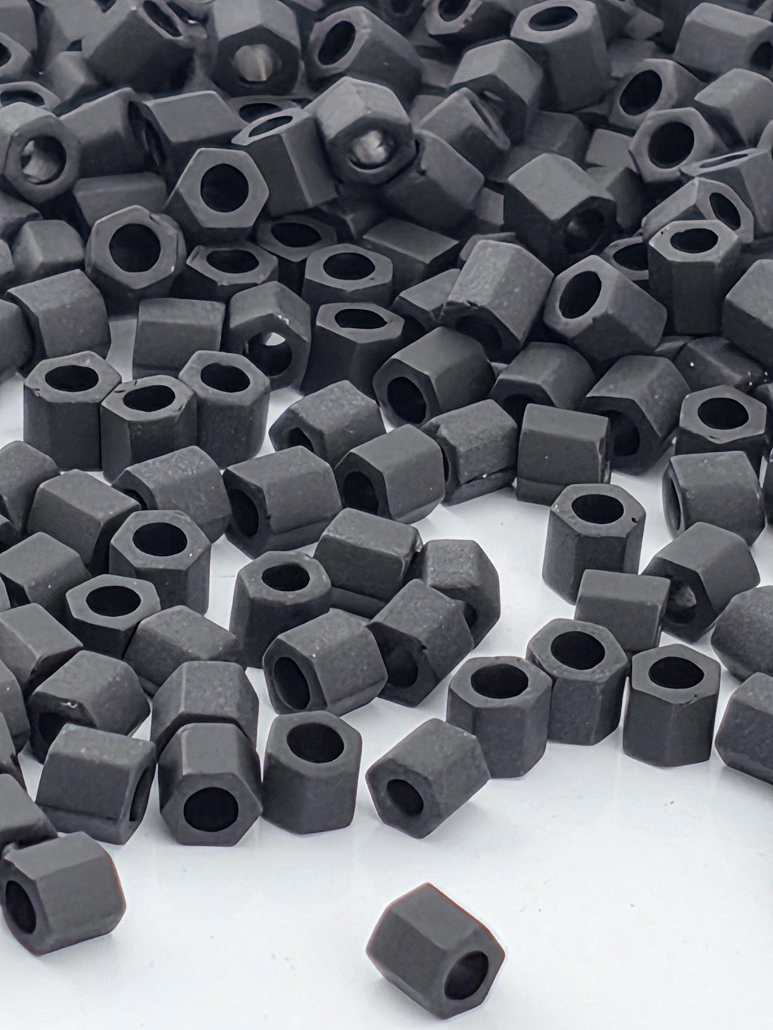 a large pile of black hexagonal nuts or bolts scattered across a white surface.