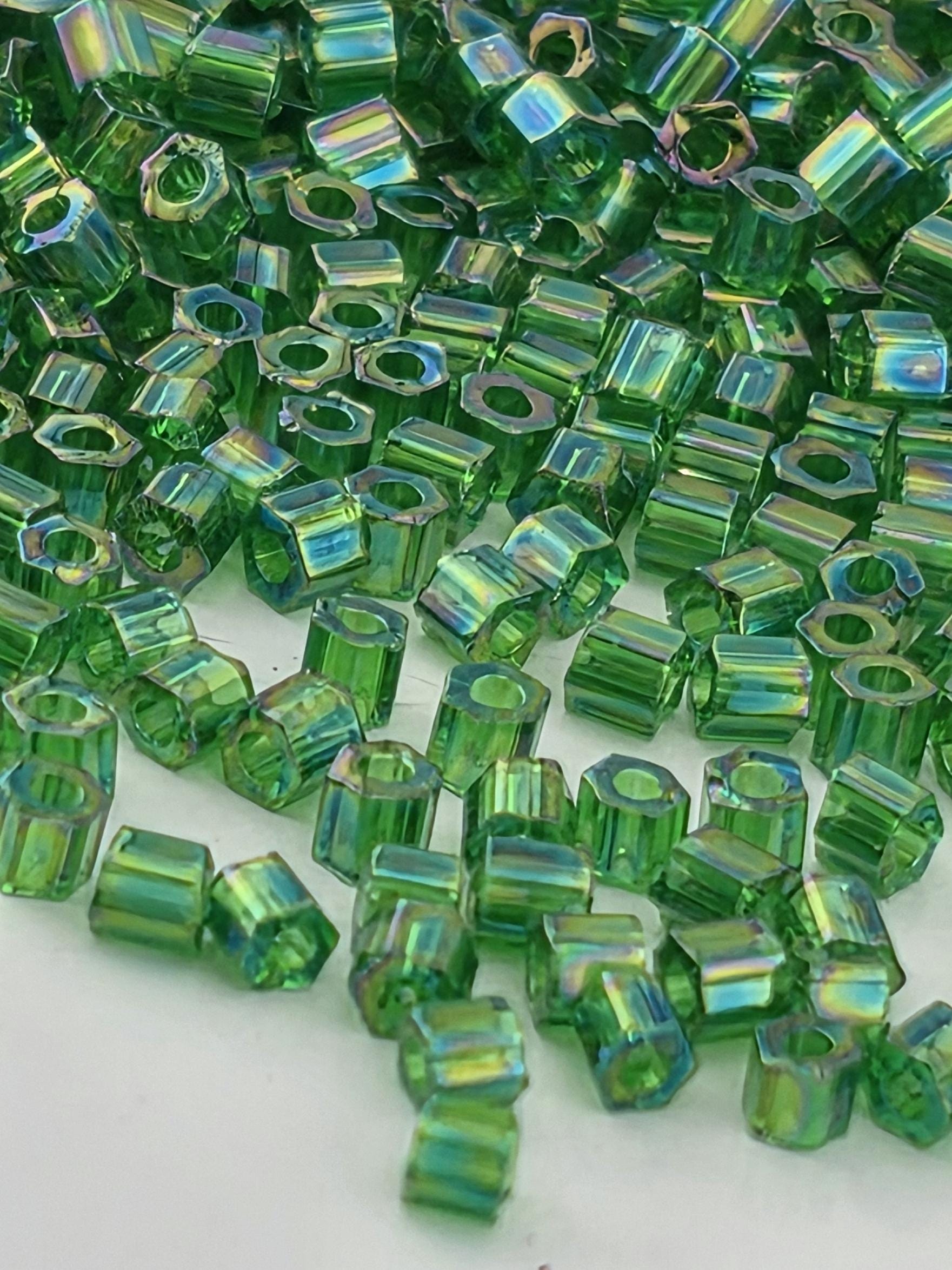 The image is a close-up of numerous green glass beads or cubes, scattered and overlapping each other.