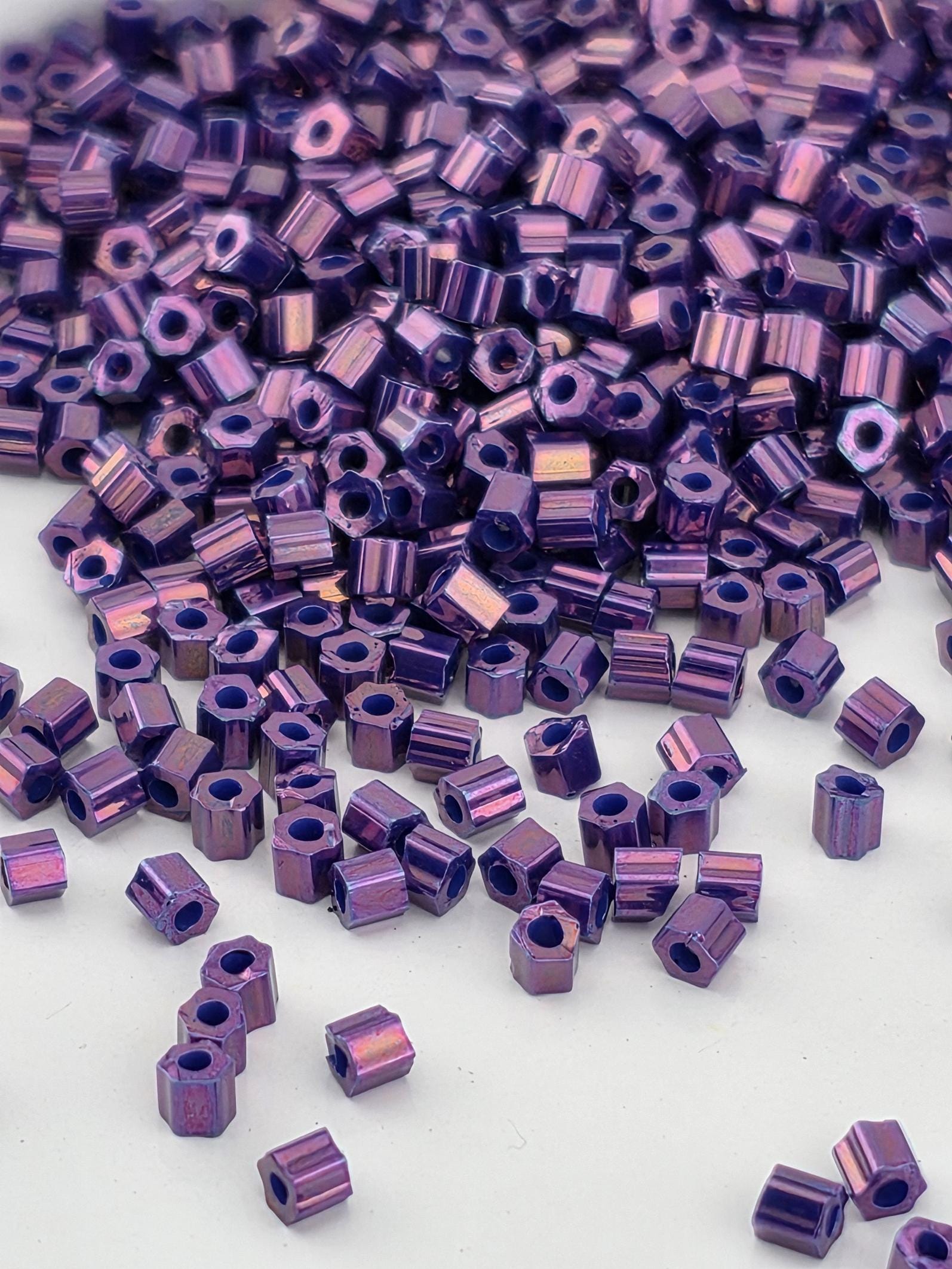 a close-up view of numerous small, purple hexagonal beads scattered across a white background.