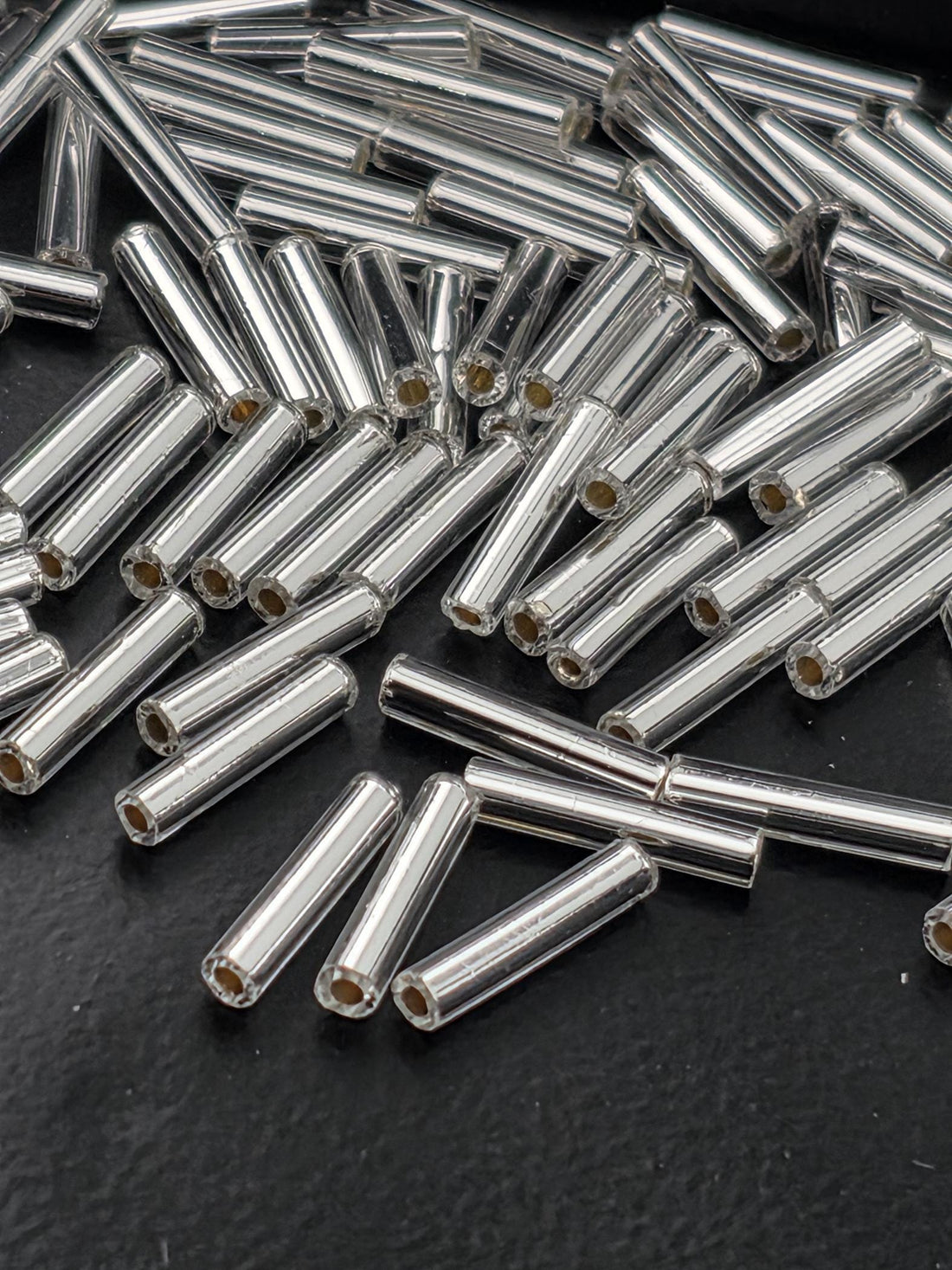 a collection of silver-colored metal rods or tubes scattered on a dark surface.