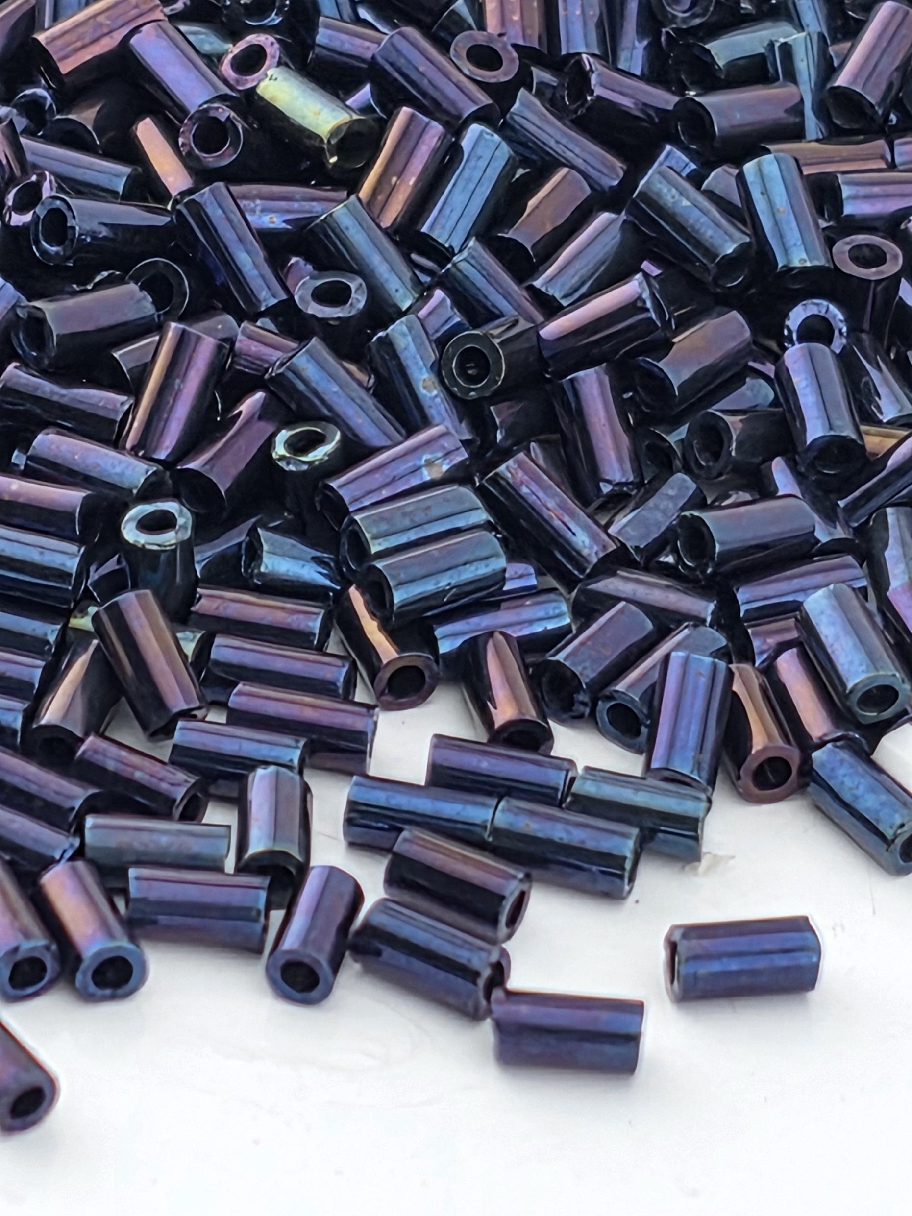 a close-up view of numerous small, cylindrical objects with a metallic, iridescent appearance. The objects are scattered across a surface, creating a visually striking and intricate pattern.