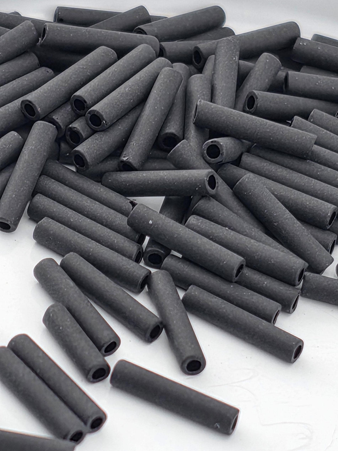 numerous black cylindrical objects, possibly metal pipes or tubes, scattered across a white surface.