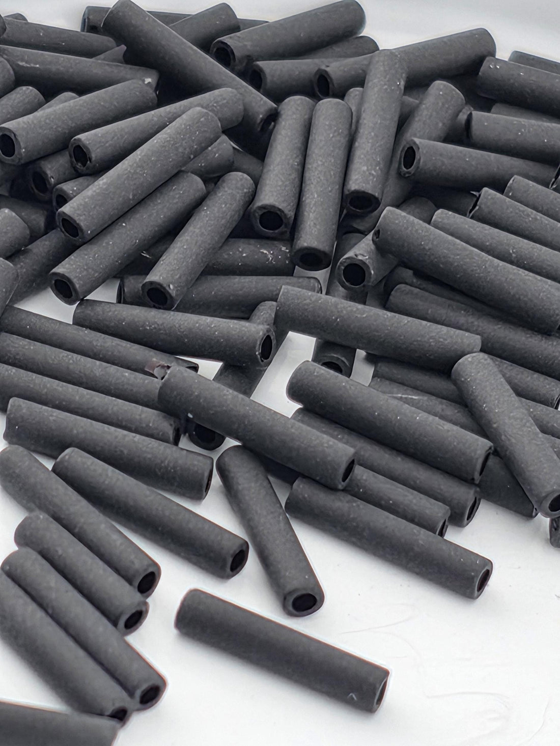 numerous black cylindrical objects, possibly metal pipes or tubes, scattered across a white surface.