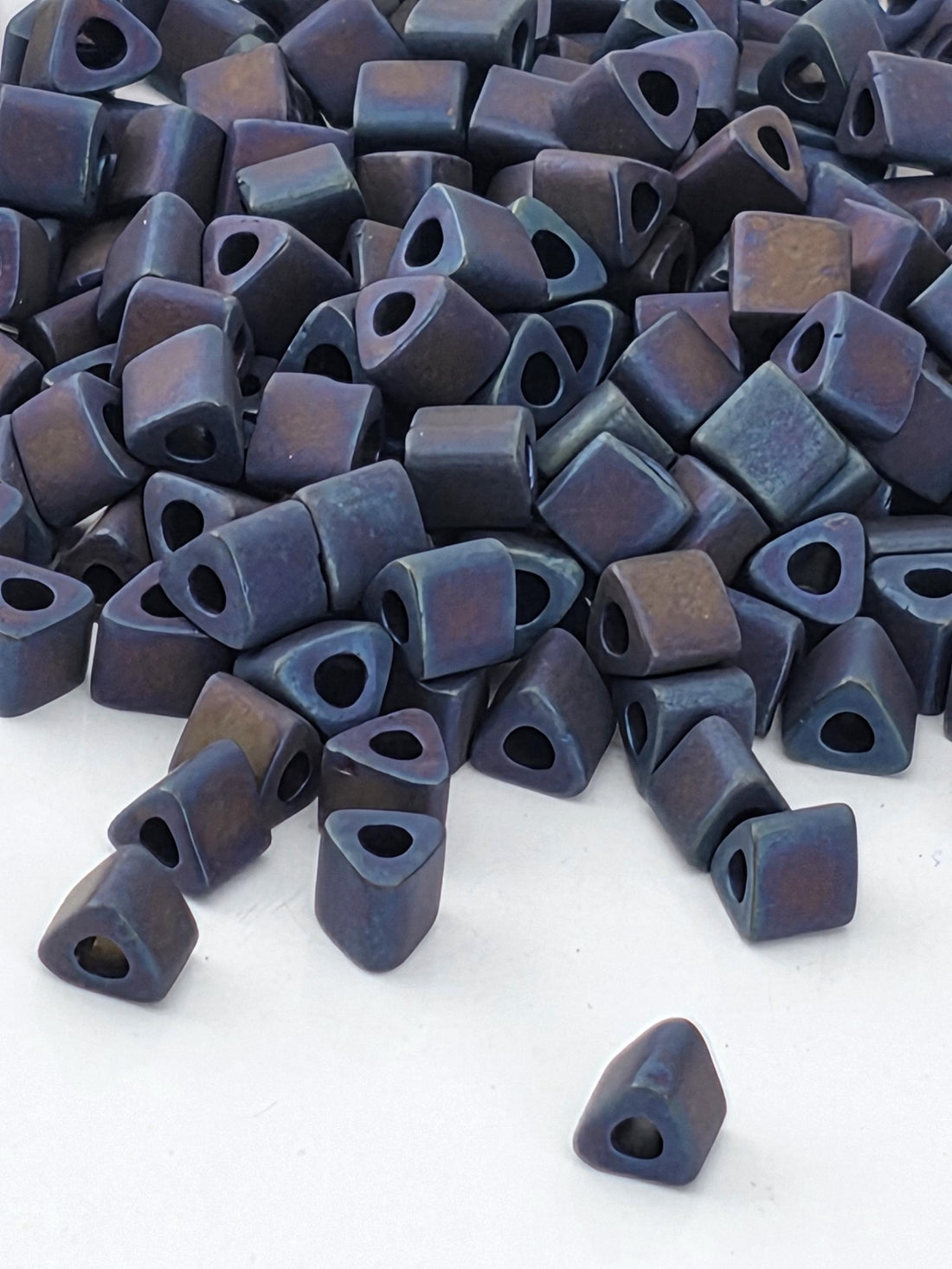 a pile of small, square-shaped objects with a dark blue or purple color, scattered on a white surface.