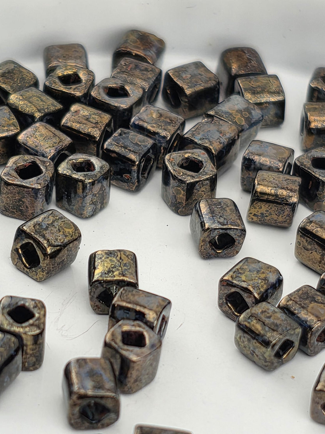 a collection of small, square-shaped metal objects with a dark, textured appearance, scattered on a white surface.