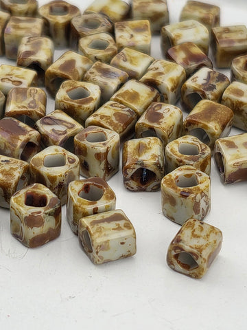 a collection of small, irregularly shaped beads or objects with a marbled or speckled appearance, scattered on a white surface.