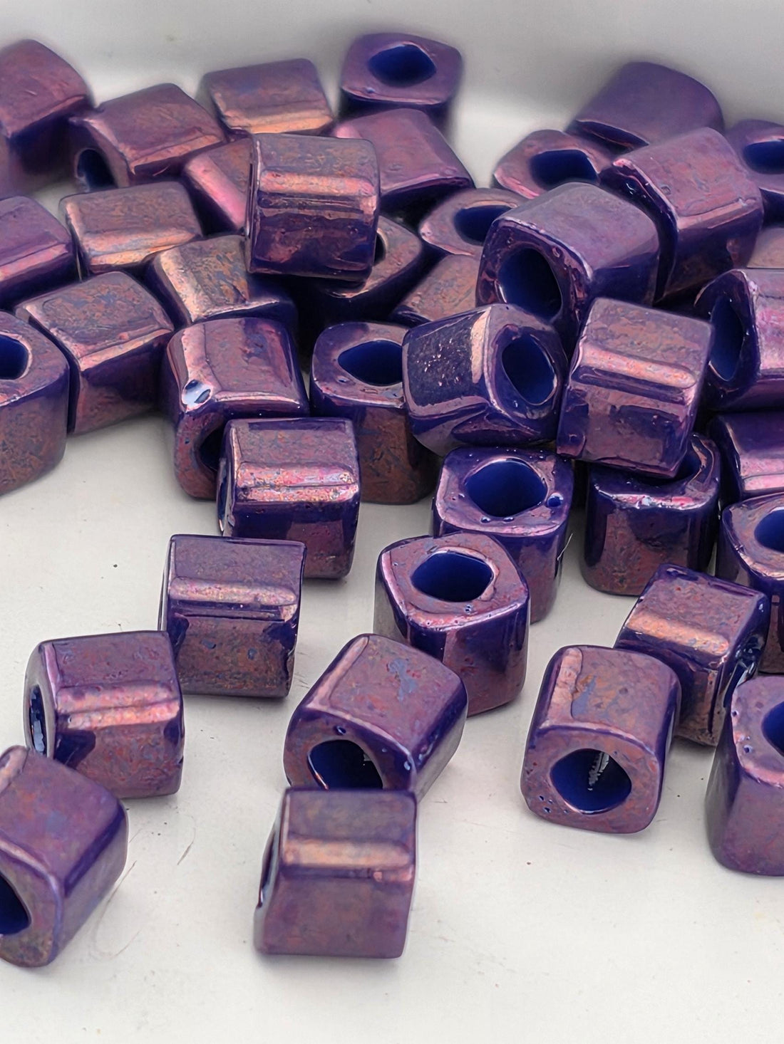a collection of small, square-shaped purple beads scattered on a white surface.