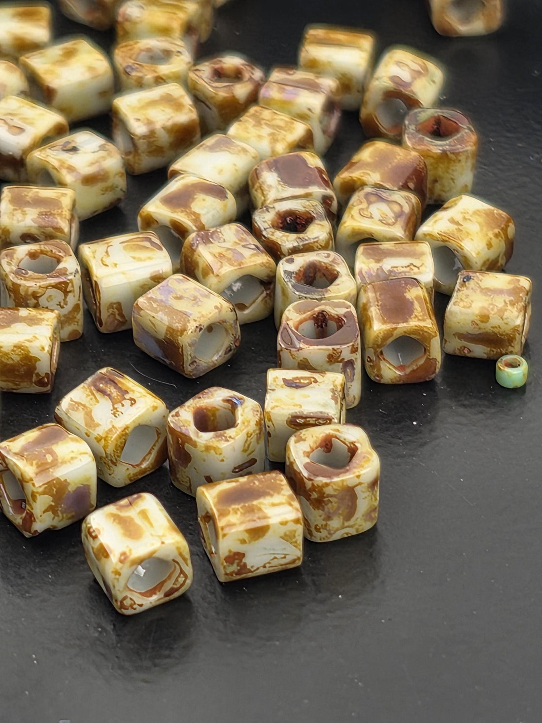 a collection of small, irregularly shaped beads or objects with a marbled or speckled appearance, scattered on a white surface.