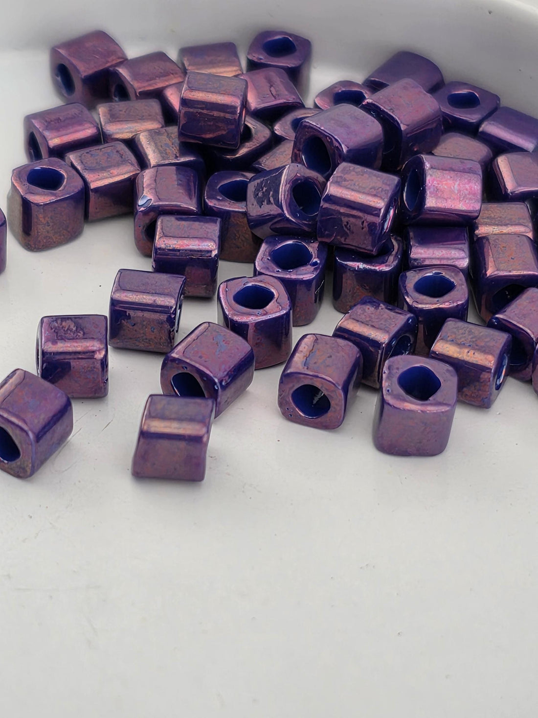 a collection of small, square-shaped purple beads scattered on a white surface.