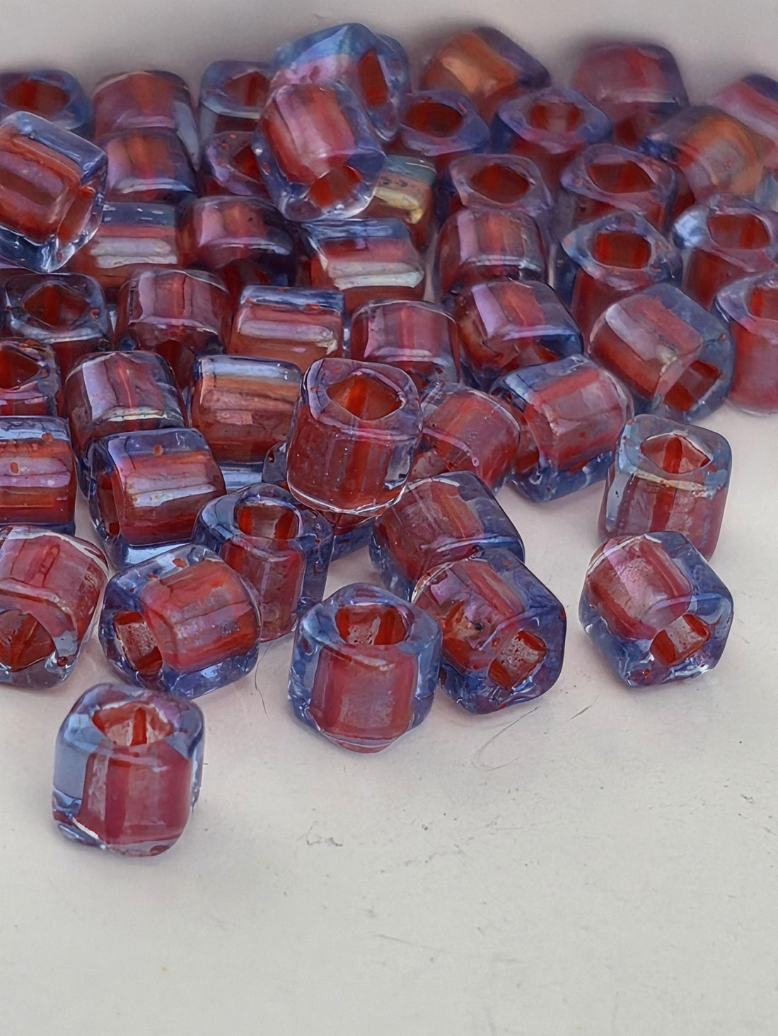 a collection of small, clear glass beads in various shades of red and blue, scattered on a white surface.
