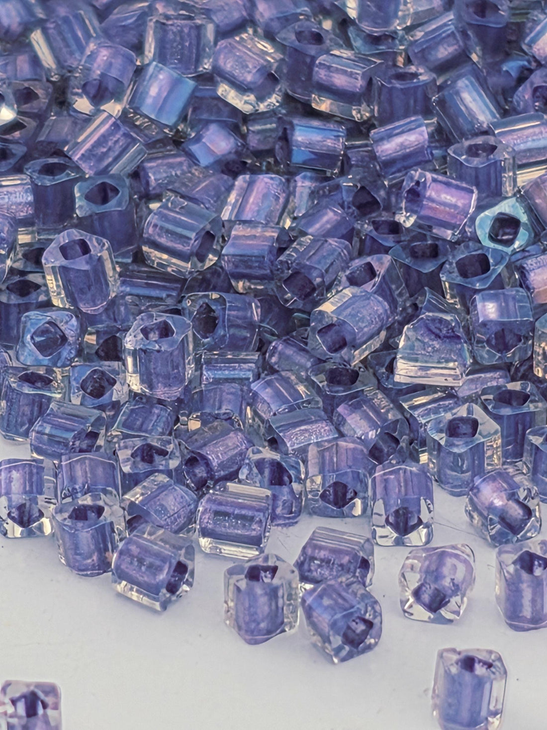 The image is a close-up of numerous small, clear beads in shades of purple, scattered across a surface.
