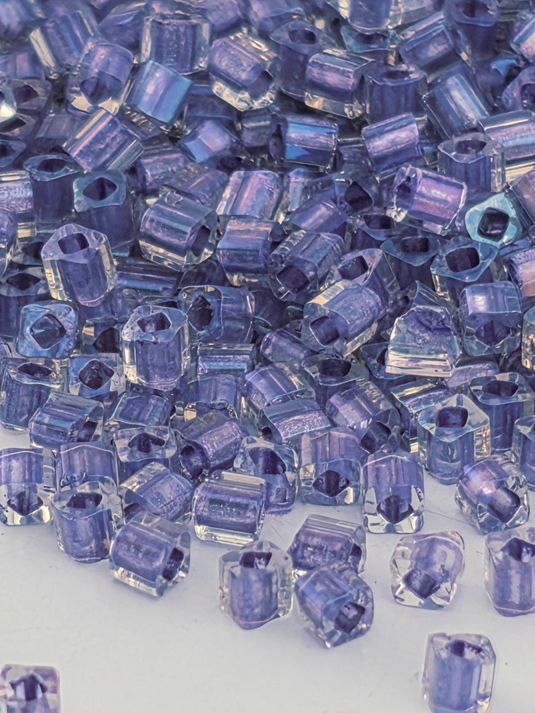 The image is a close-up of numerous small, clear beads in shades of purple, scattered across a surface.