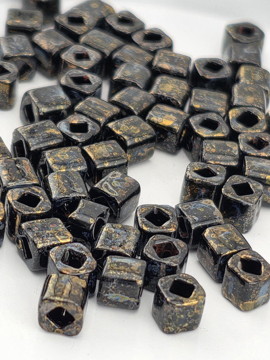 a collection of small, square-shaped metal pieces with a dark, textured appearance. The pieces are scattered across a white surface, creating a visually striking contrast.