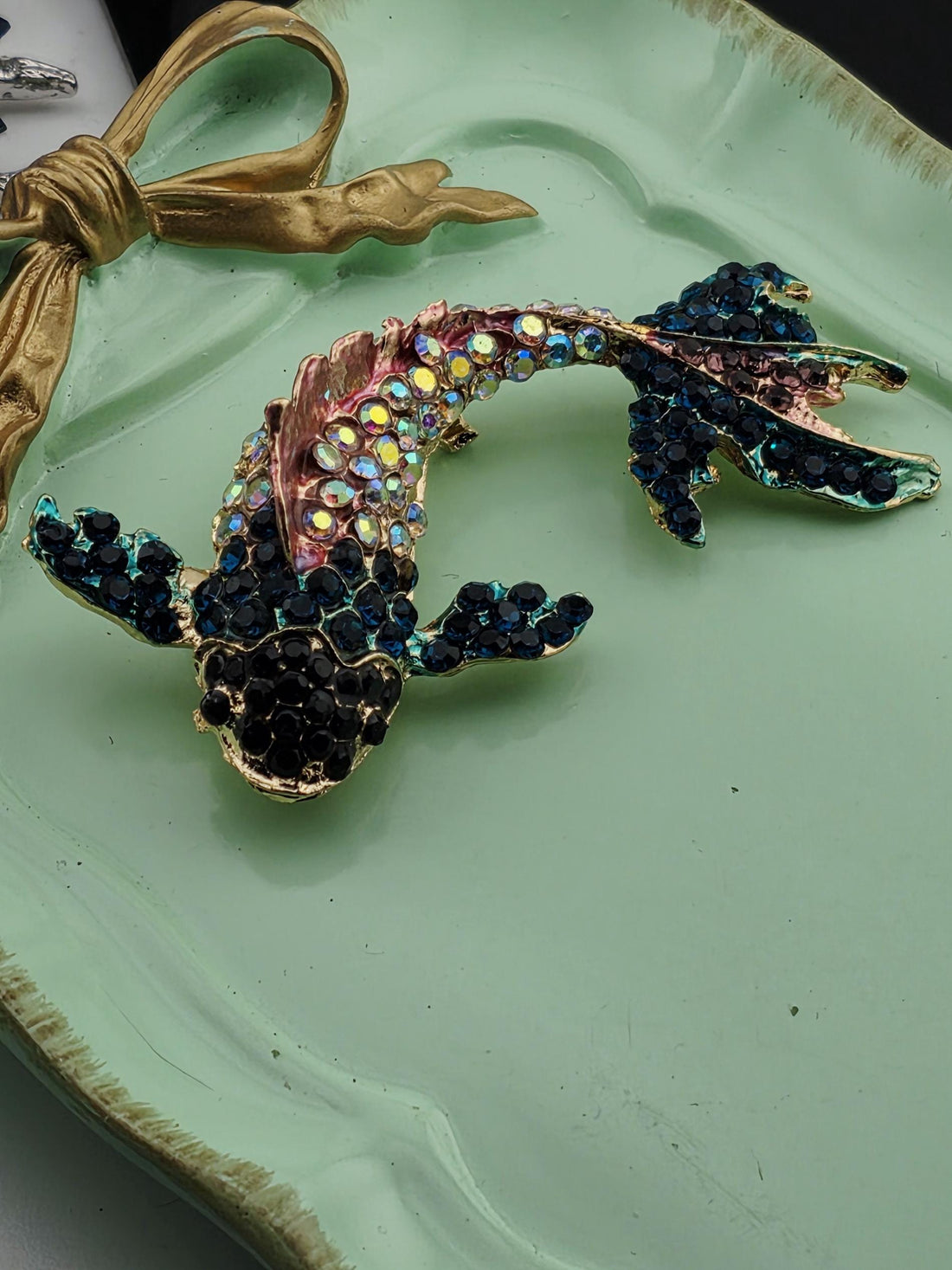 A decorative fish brooch with a colorful, sparkling design is displayed in a white ornate frame.