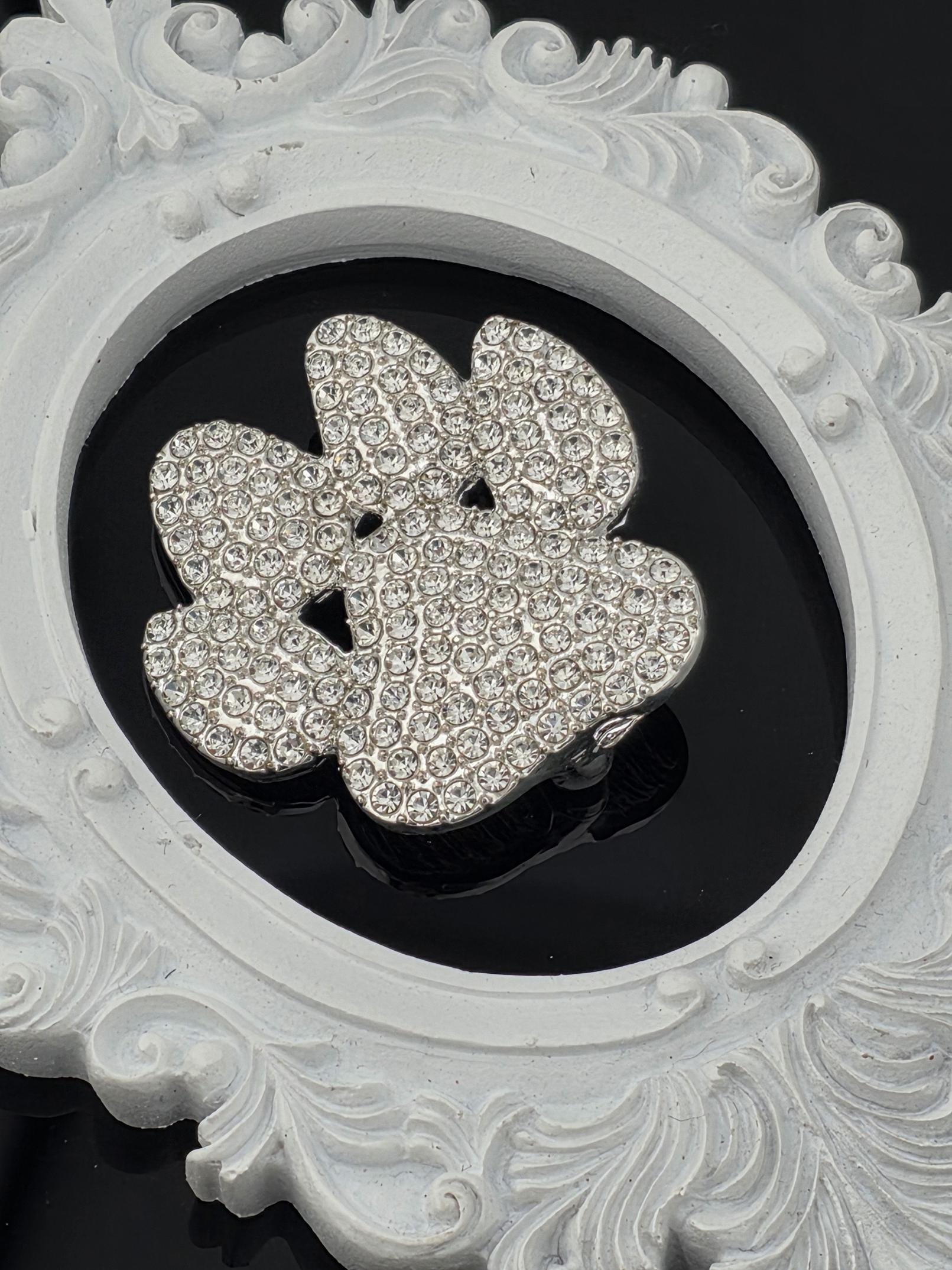 A close-up image of a white ornate frame with a large, sparkling crystal flower design in the center.