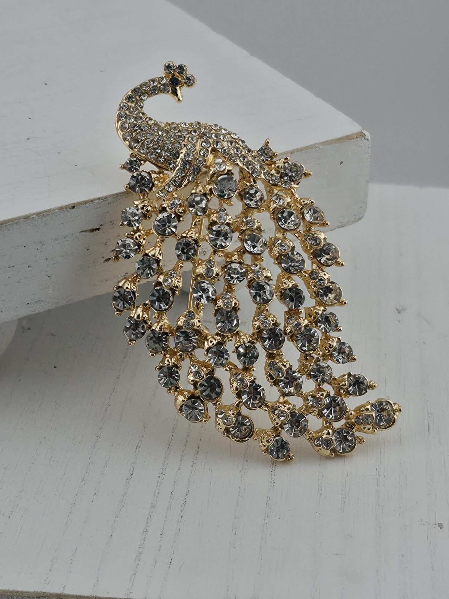 A decorative brooch in the shape of a peacock, adorned with numerous small diamonds in various colors.