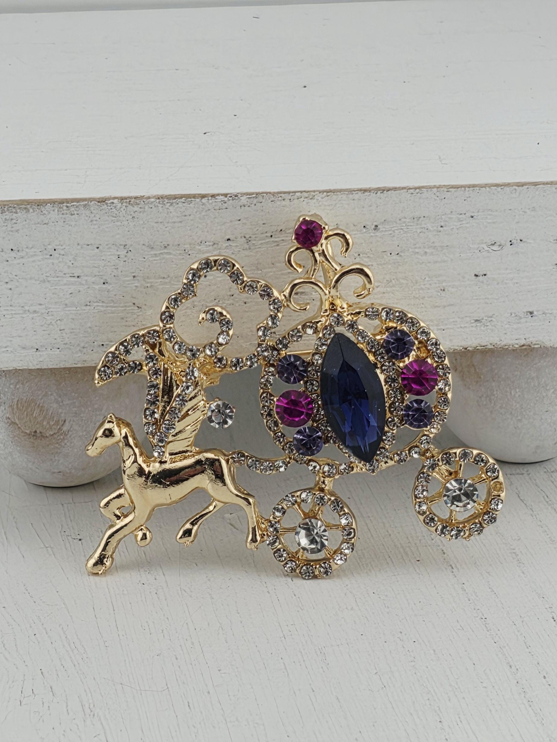 A decorative brooch with a combination of gold, purple, and blue gemstones, as well as a gold animal figure, is displayed against a white background.