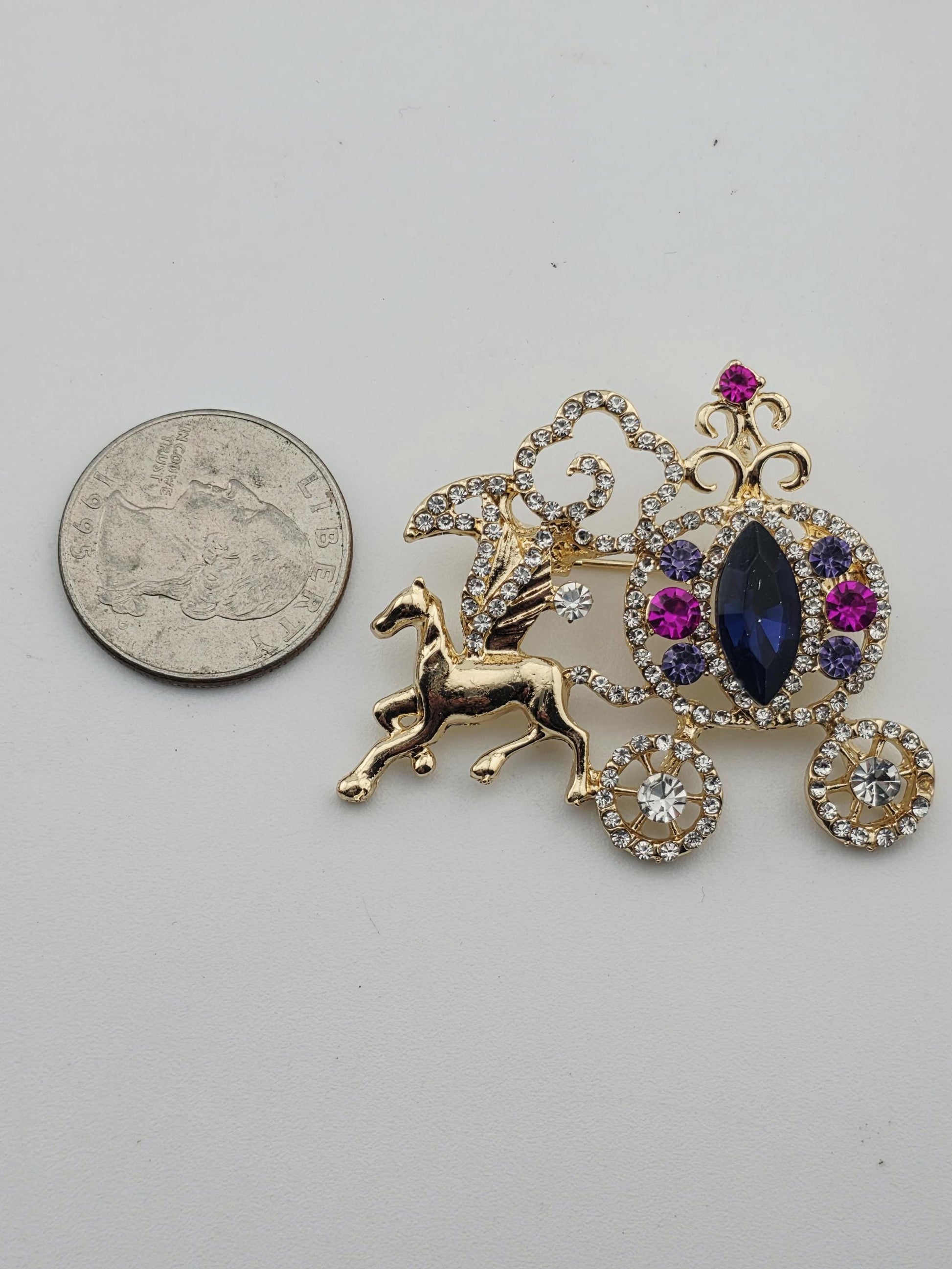 a decorative piece of jewelry, including a pendant and a winged horse, placed next to a United States quarter.