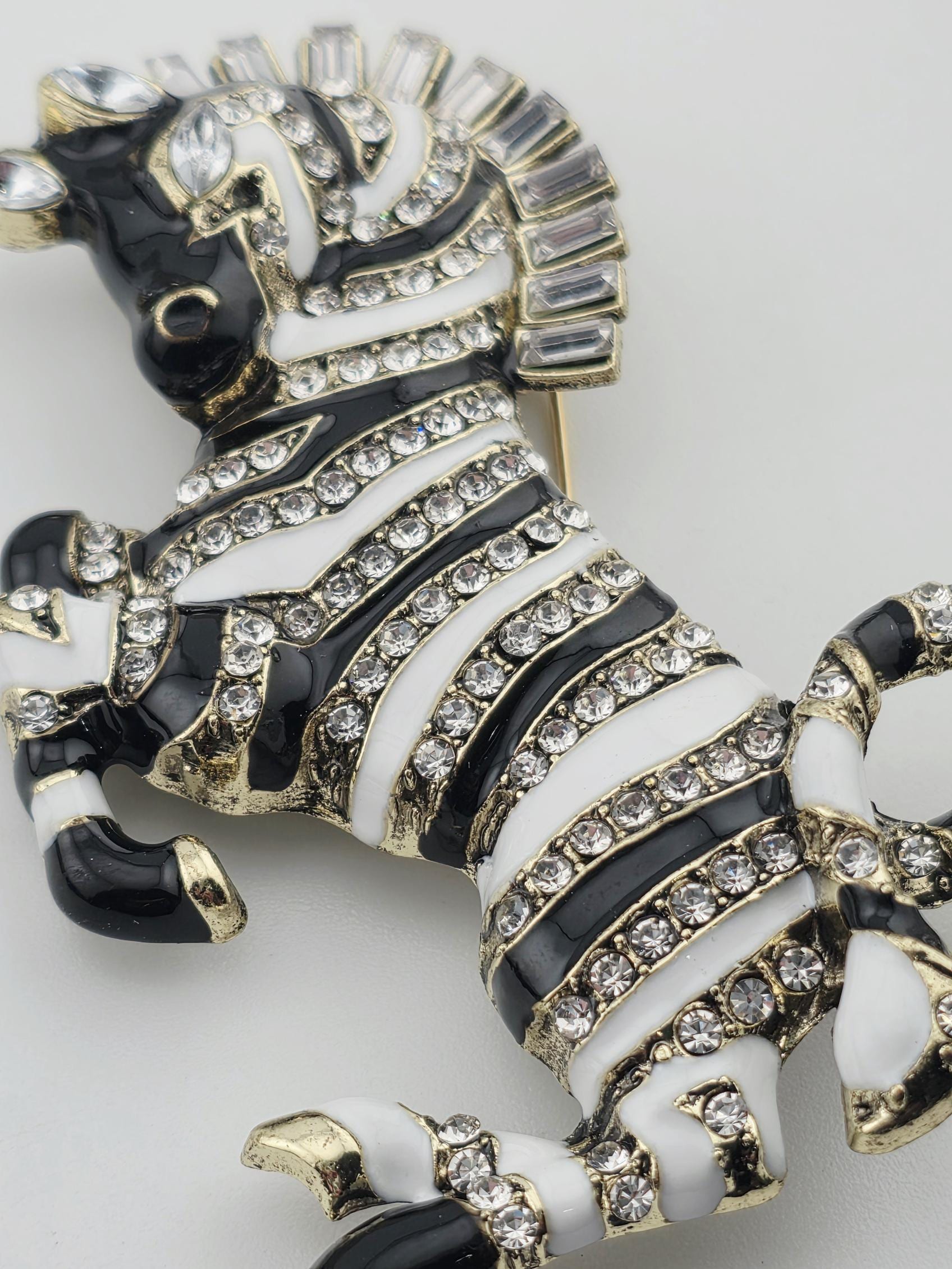 A decorative zebra brooch with black and white stripes and gold accents, adorned with numerous small diamonds.