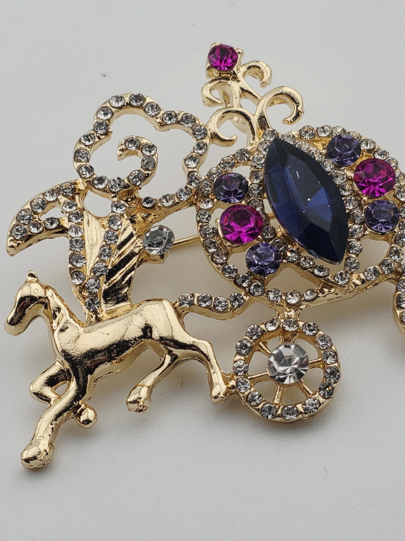 A decorative brooch with a combination of gold, purple, and blue gemstones, as well as a central gold-colored animal-shaped charm.