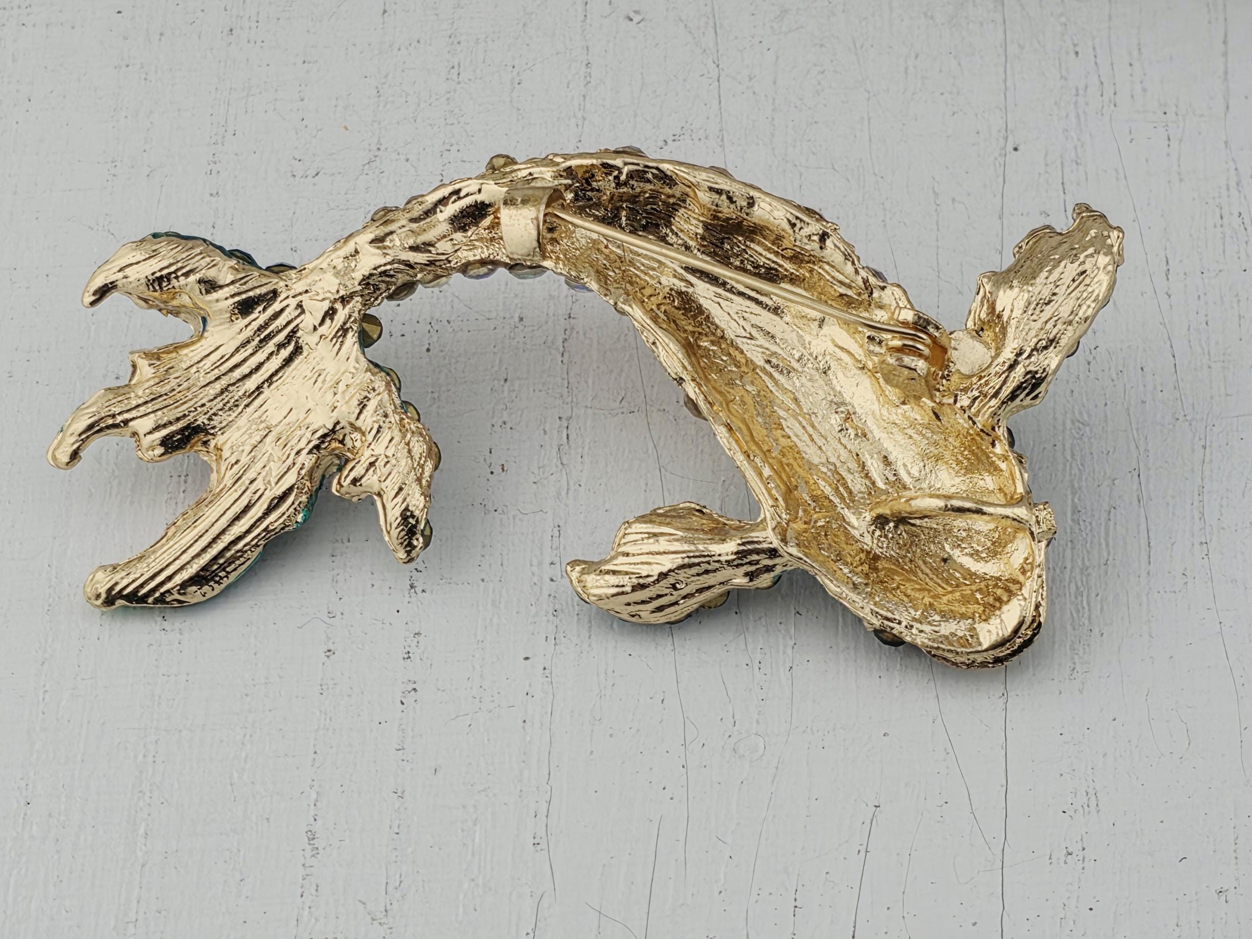A gold-colored fish brooch is displayed against a white background.