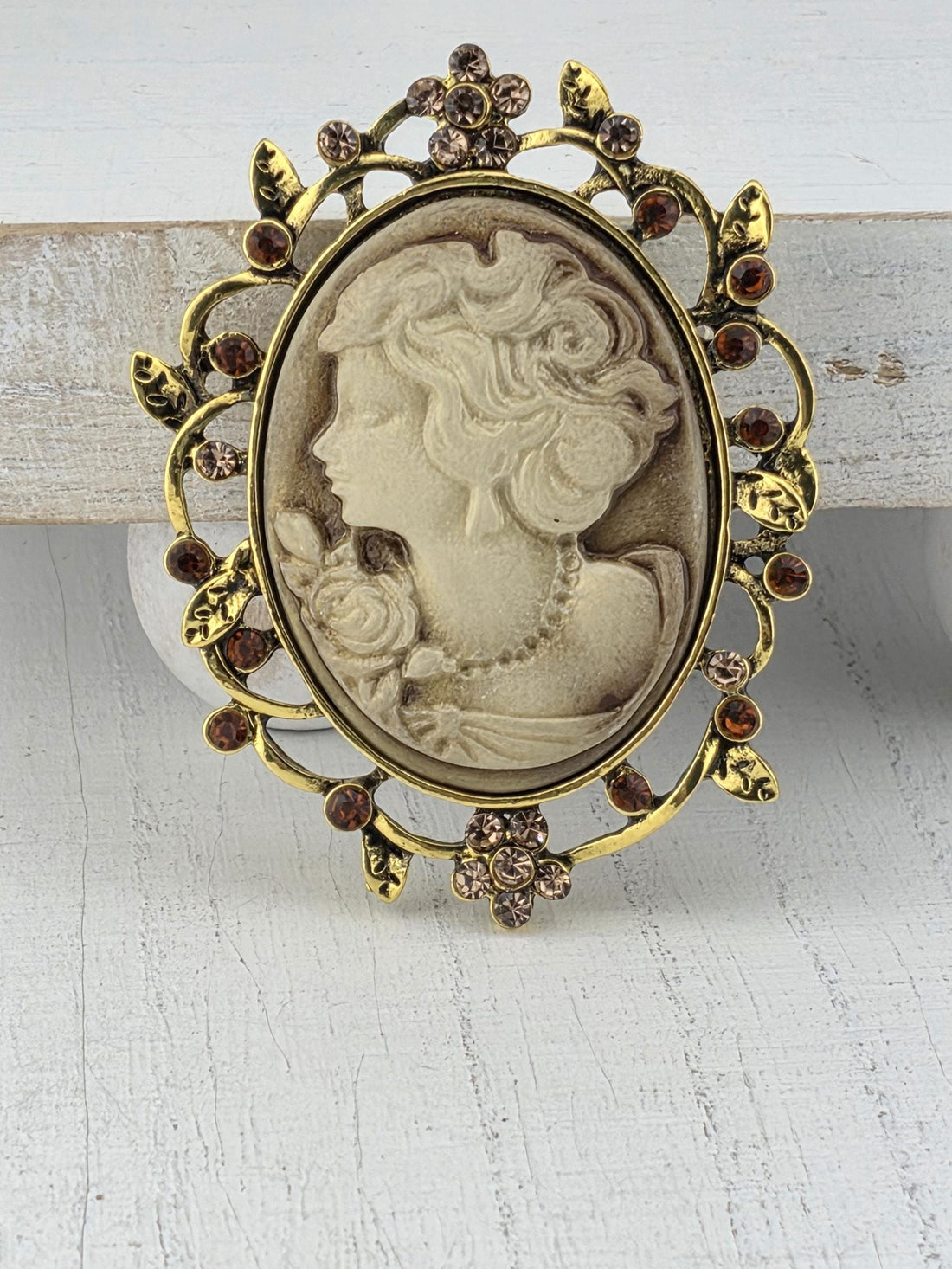 A decorative brooch featuring a carved profile of a woman's face, adorned with small gemstones and intricate metalwork.