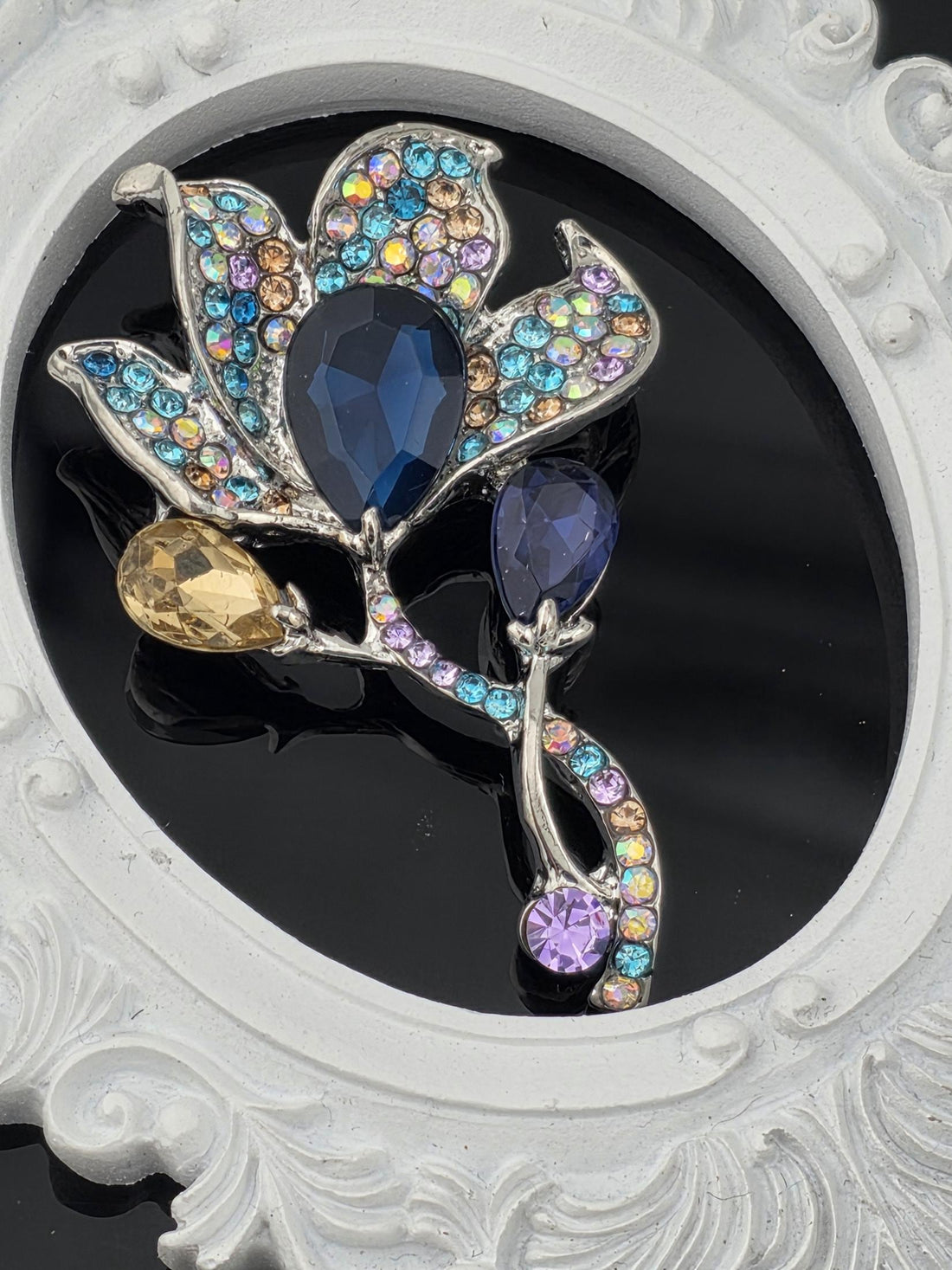 A decorative brooch with a floral design and colorful gemstones, including blue, purple, and yellow stones, set against a black background.