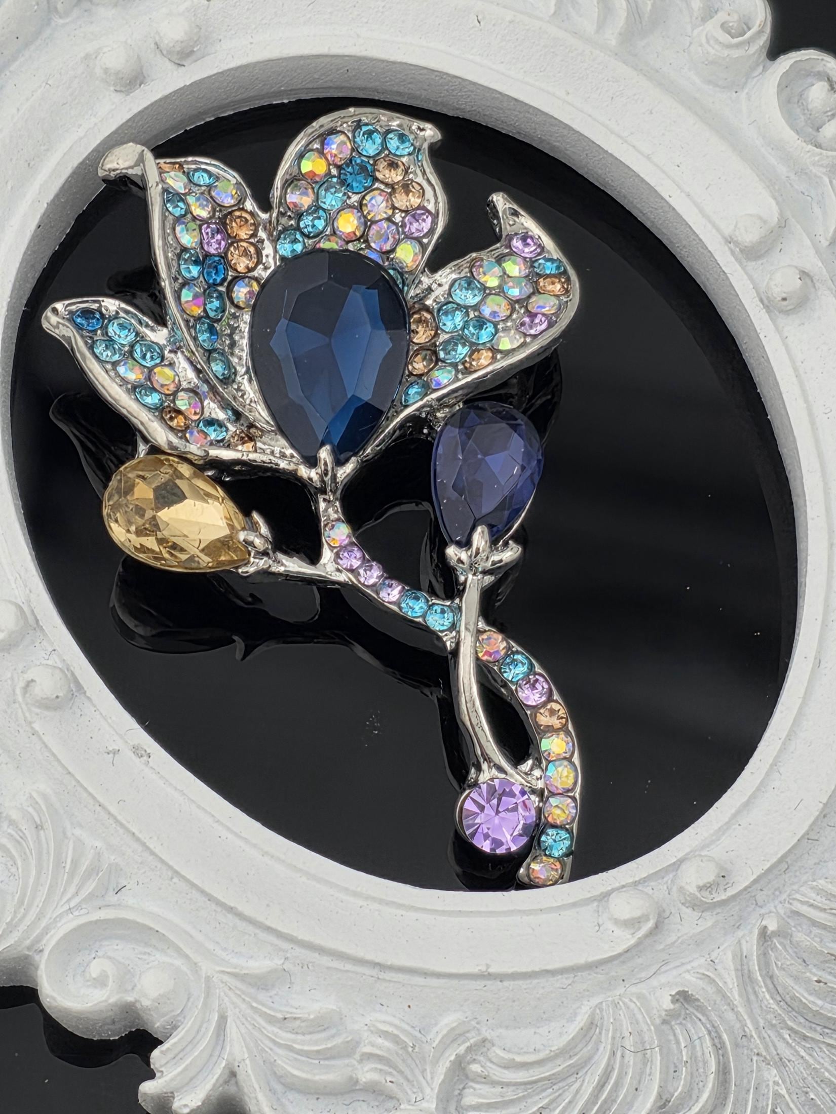 A decorative brooch with a floral design and colorful gemstones, including blue, purple, and yellow stones, set against a black background.