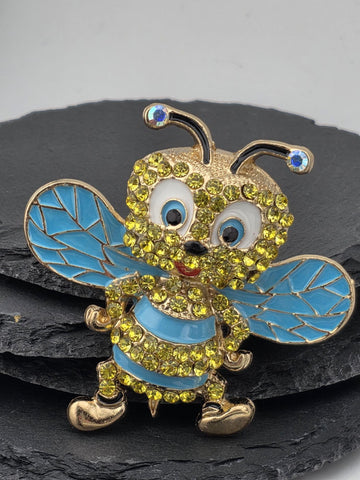 A decorative pin featuring a blue and yellow bee-like creature with sparkling rhinestones and gold accents.
