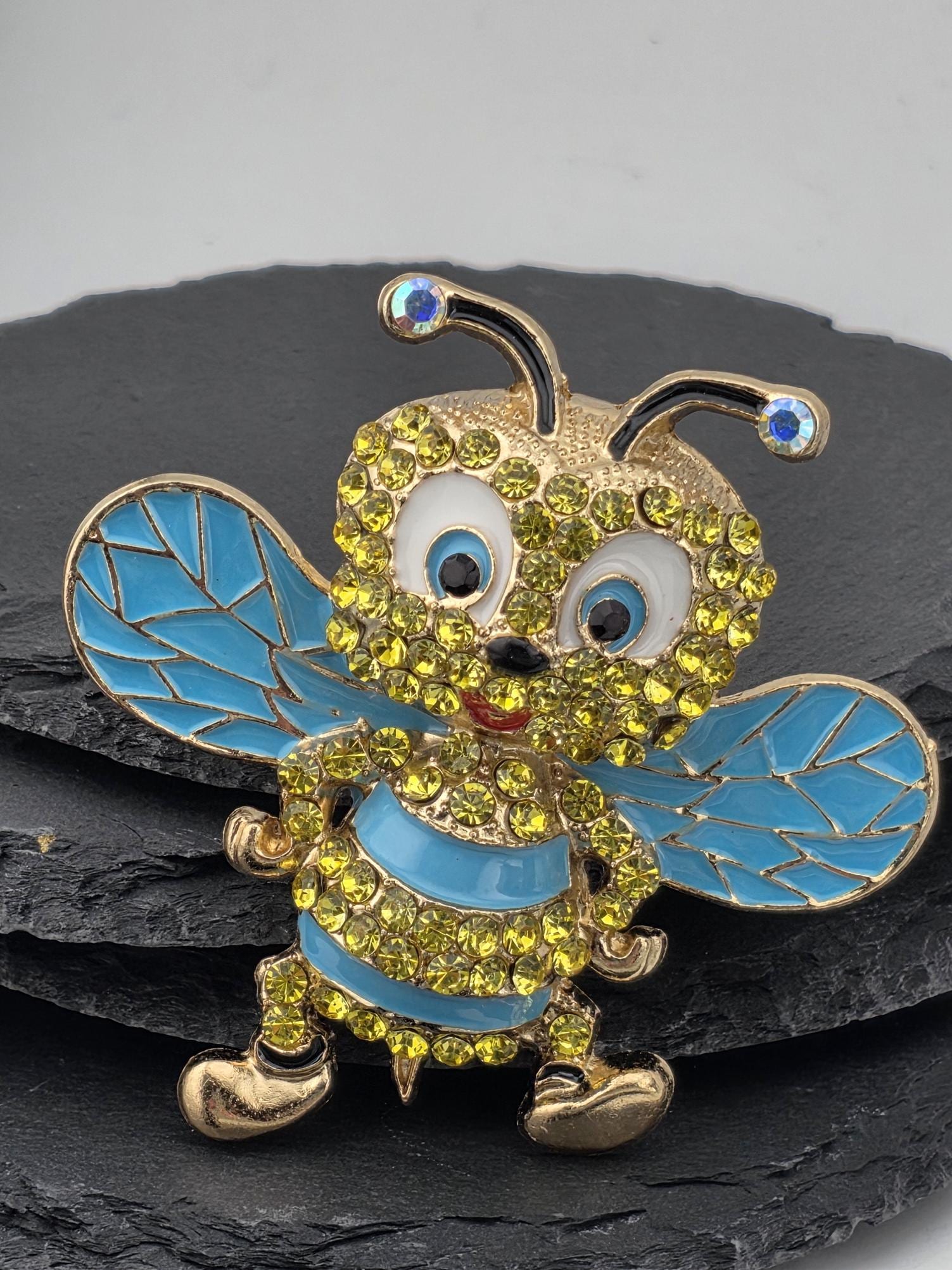 A decorative pin featuring a blue and yellow bee-like creature with sparkling rhinestones and gold accents.