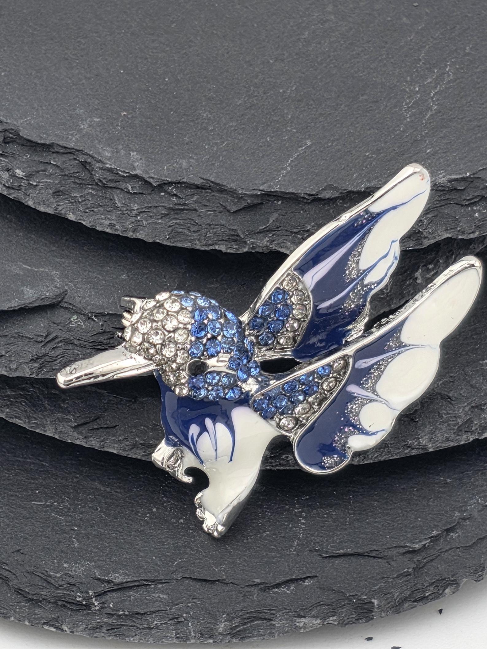 A decorative brooch in the shape of a dragonfly, with blue and white colors and sparkling gemstones.