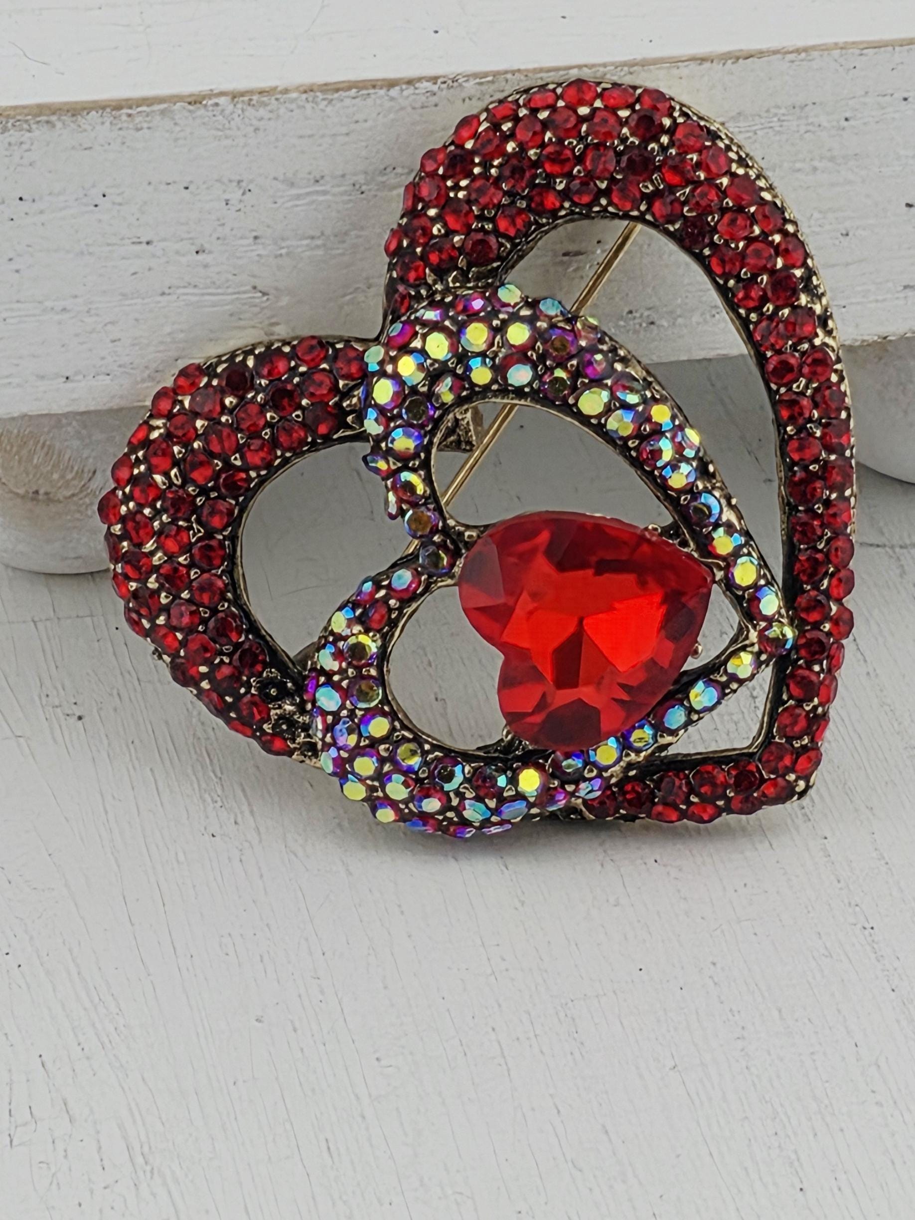 A decorative red gemstone brooch with a heart-shaped design and sparkling rhinestones.