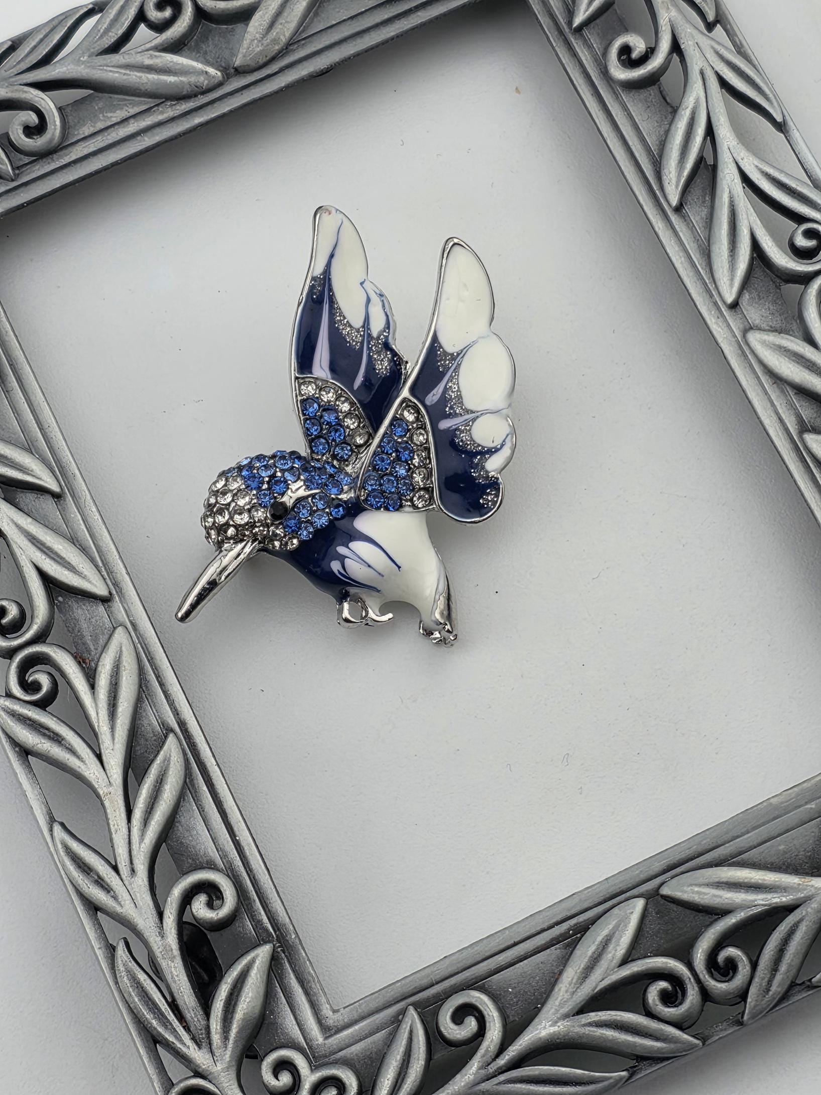 A decorative silver frame with a butterfly brooch in the center, placed on a white background.