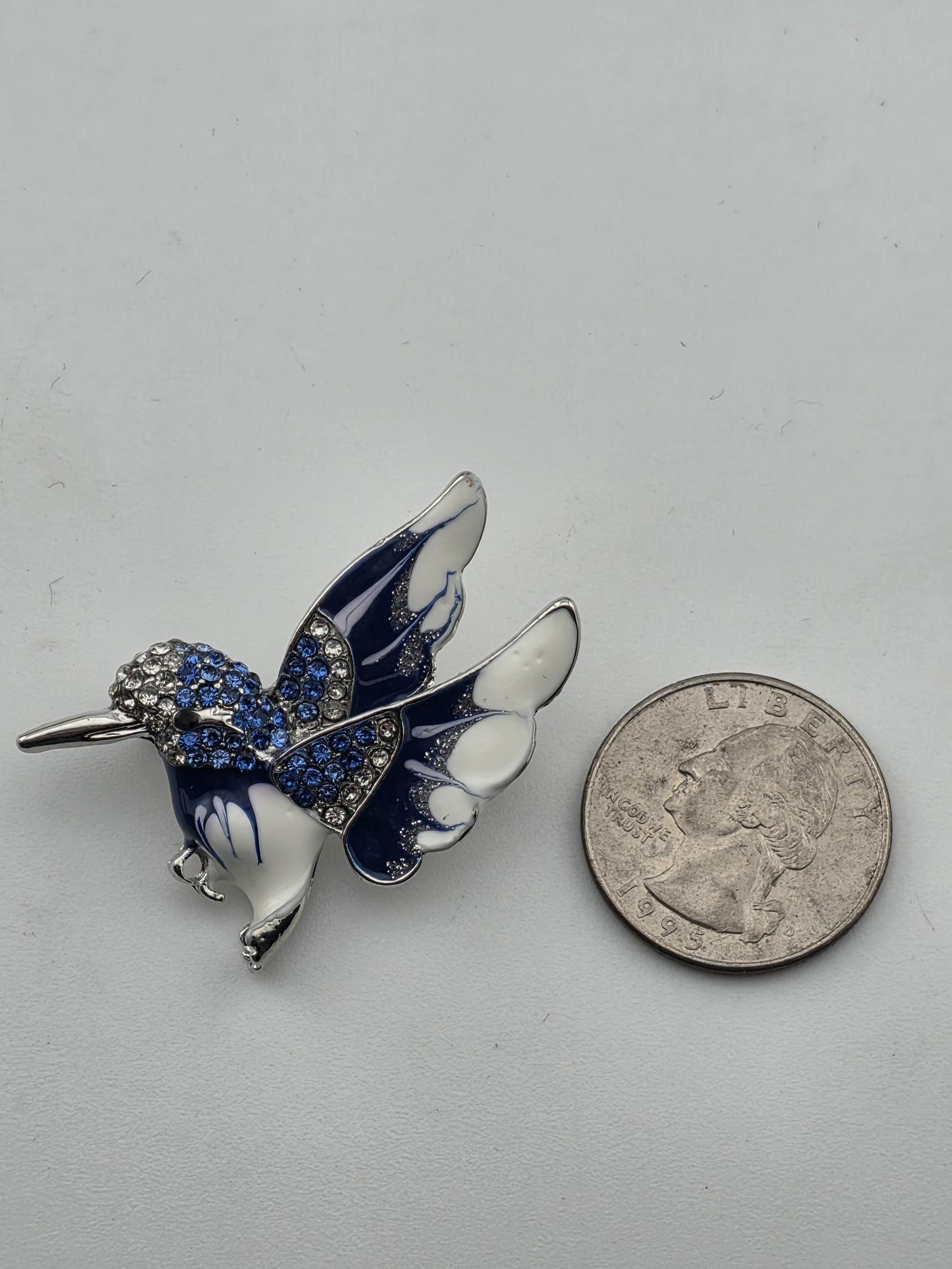 A silver butterfly brooch with blue and white accents, adorned with sparkling stones, is placed next to a United States quarter coin.