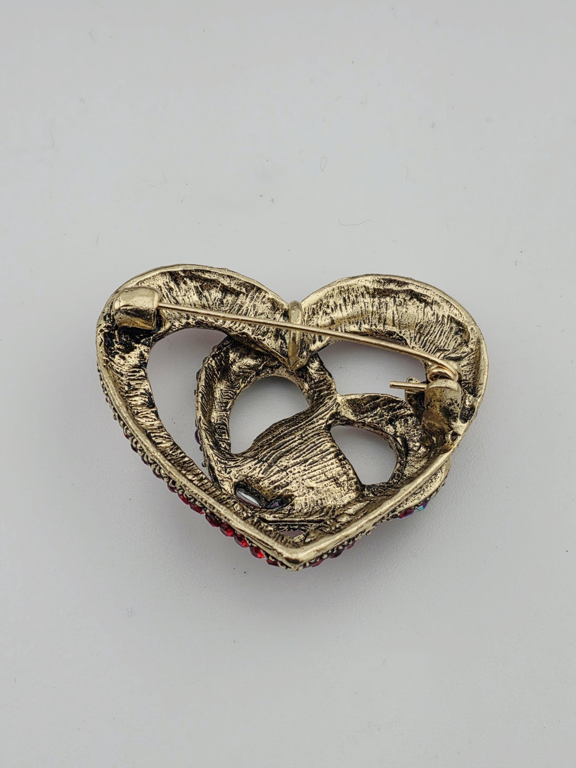 A gold-colored brooch with a heart-shaped design and red gemstones.