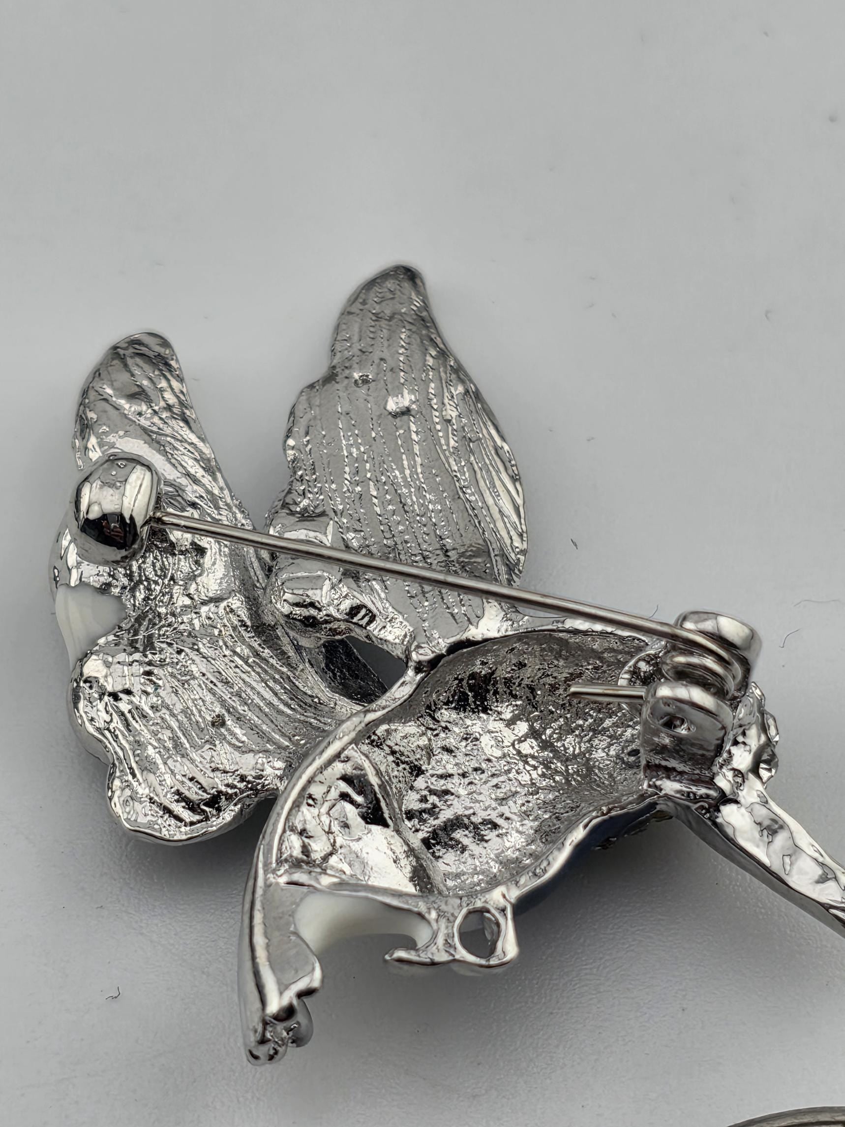 A close-up view of a silver-colored metal brooch or pin with a textured, embossed surface.