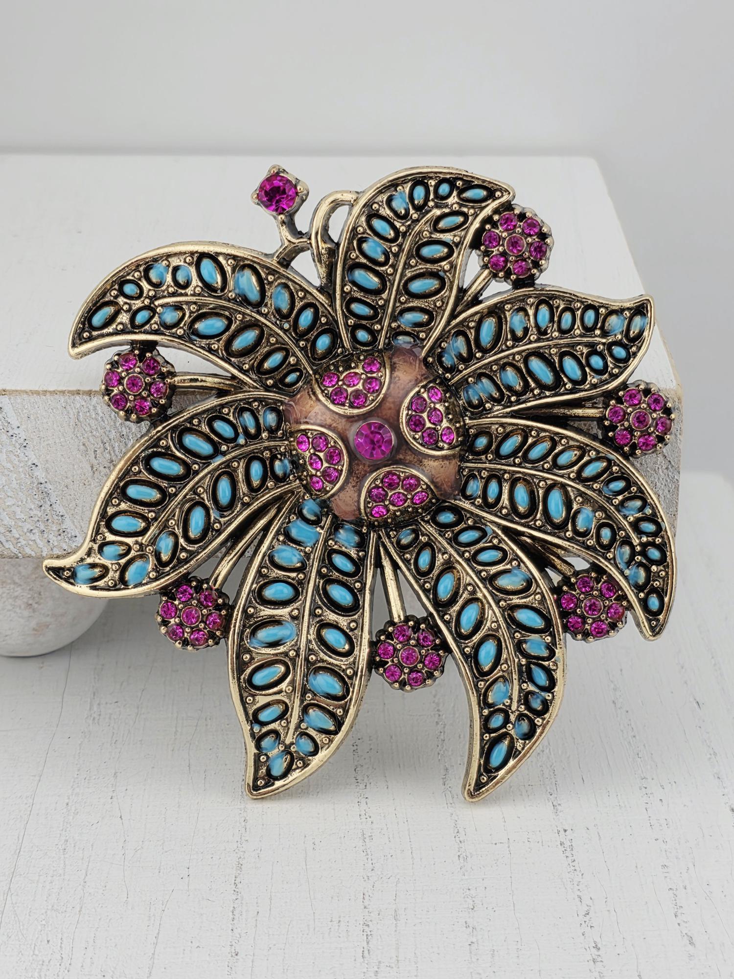 A decorative brooch with a floral design, featuring a combination of blue and purple gemstones and a metallic gold-colored center.