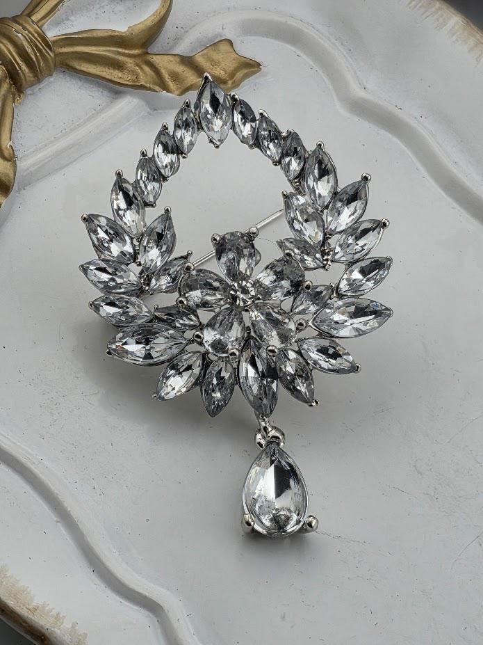 A silver brooch with a large, sparkling crystal design, featuring a dangling crystal element.
