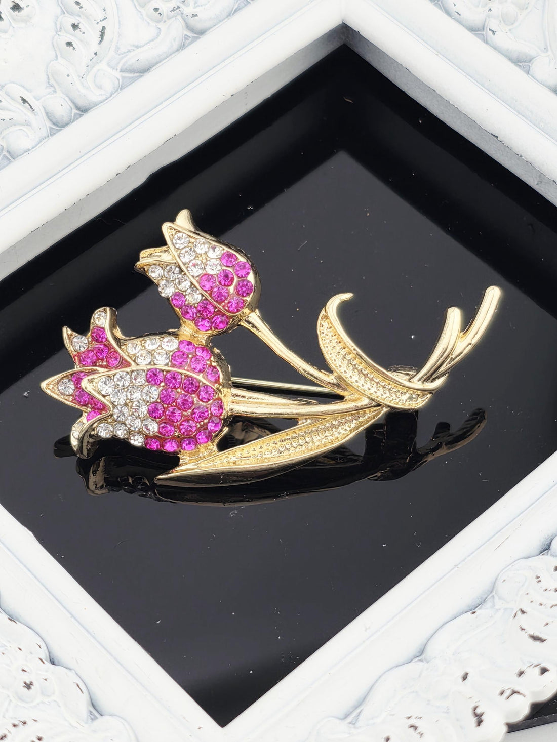 A decorative brooch with a floral design, featuring pink and white flowers with sparkling gemstones.