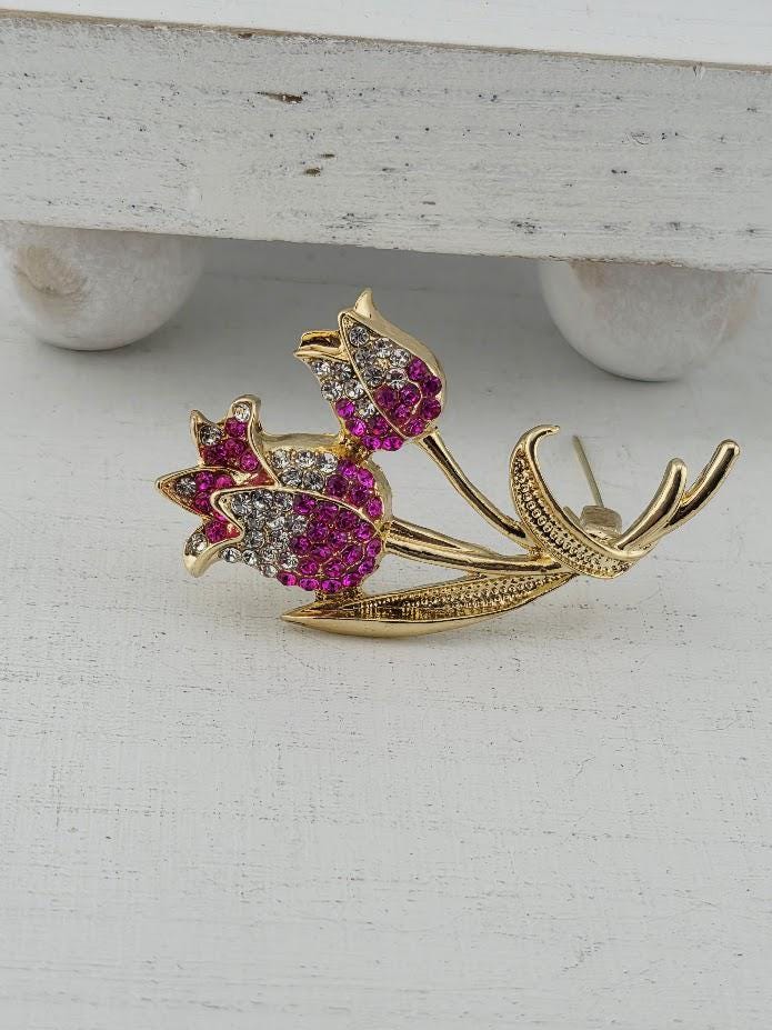 A decorative brooch with a floral design, featuring pink and white flowers with sparkling gemstones.